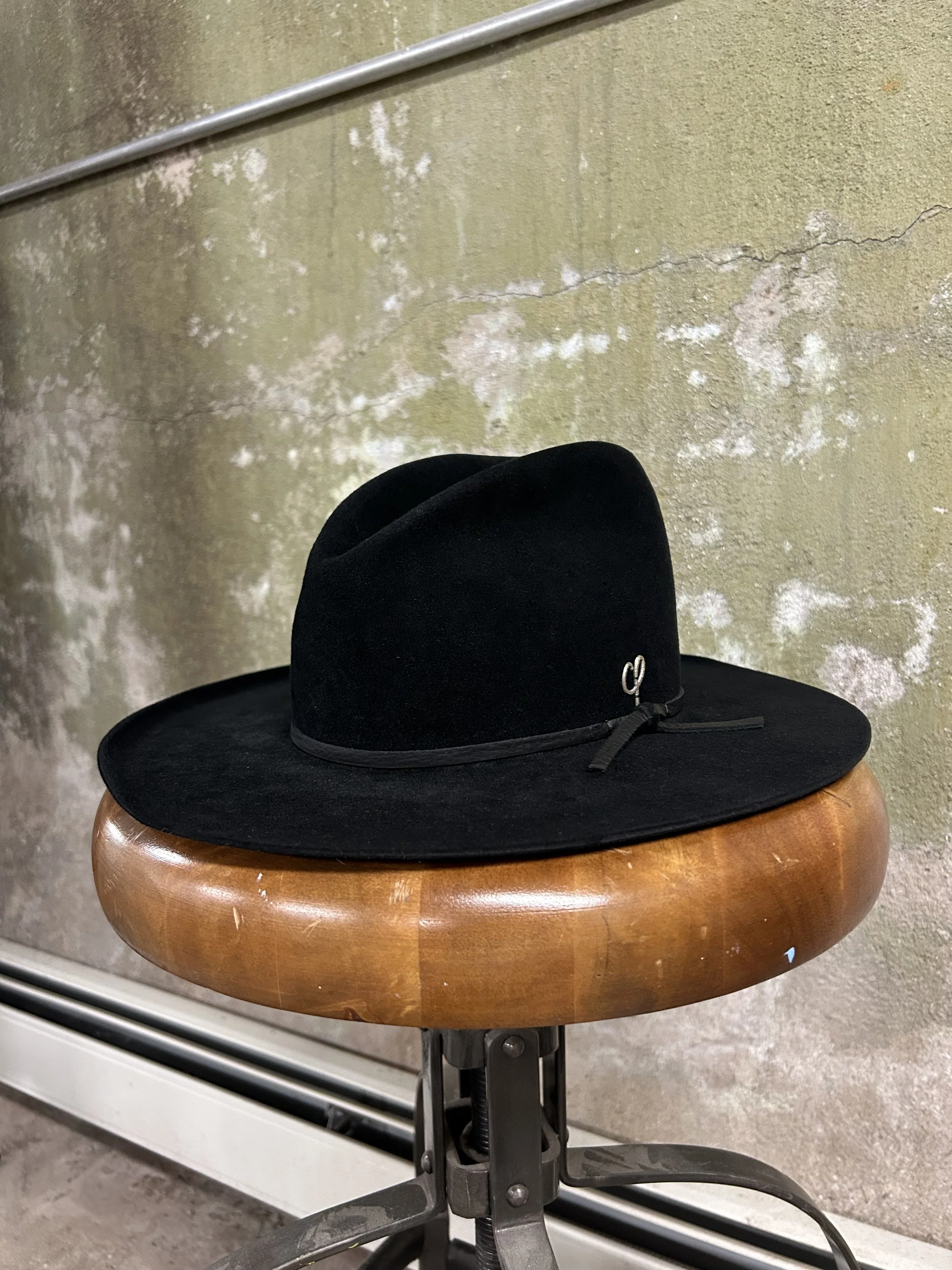 Black wide-brimmed hat on a round wooden stool against a weathered green wall.