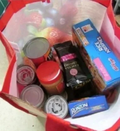 A shopping bag filled with canned goods, a box of Rice Krispies, and other grocery items.