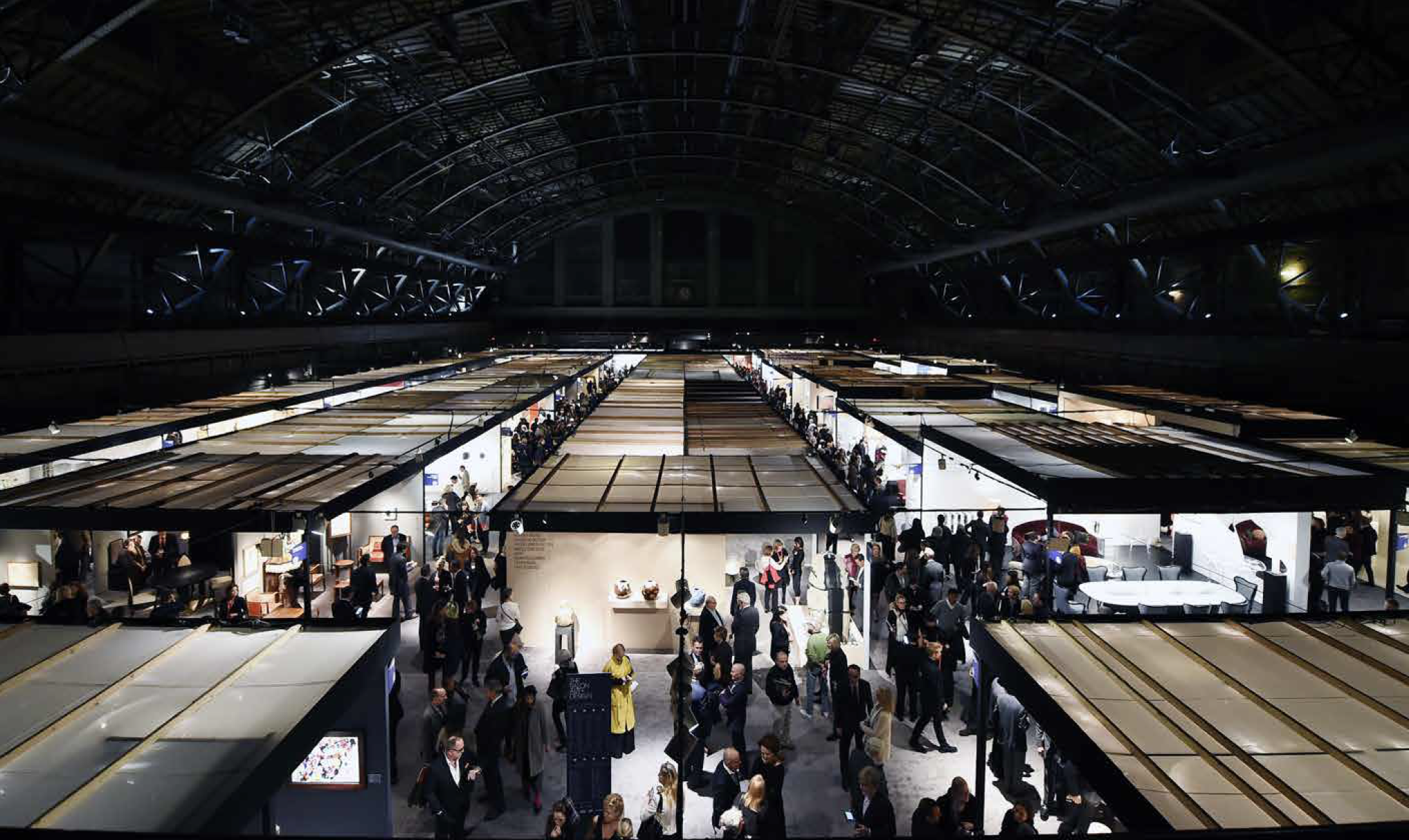 View of a busy art fair exhibition hall with numerous booths and attendees browsing artworks and displays.
