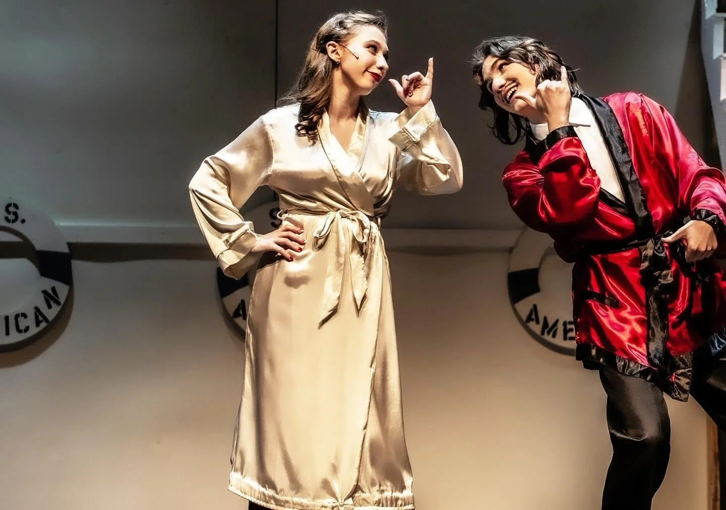 Grace playing Reno Sweeney from Anything Goes broadway musical on stage in satin robes, one in cream and the other in red, performing in front of American flag-themed balloons.