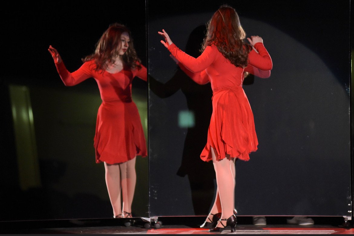 Cassie in  the mirror in A Chorus Line.  Photo of Cassie during Music and the mirror. A woman in a red dress standing in front of a mirror, looking at her reflection on stage.