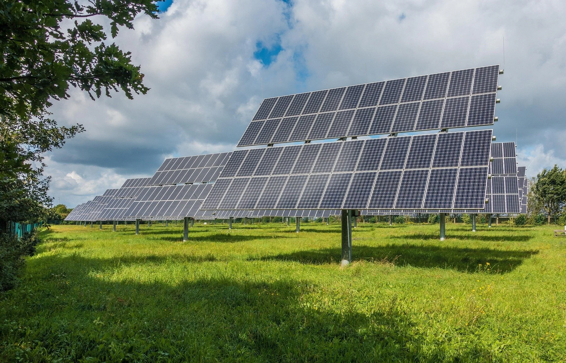 Multiple solar panels installed on a grassy field beneath a partly cloudy sky.