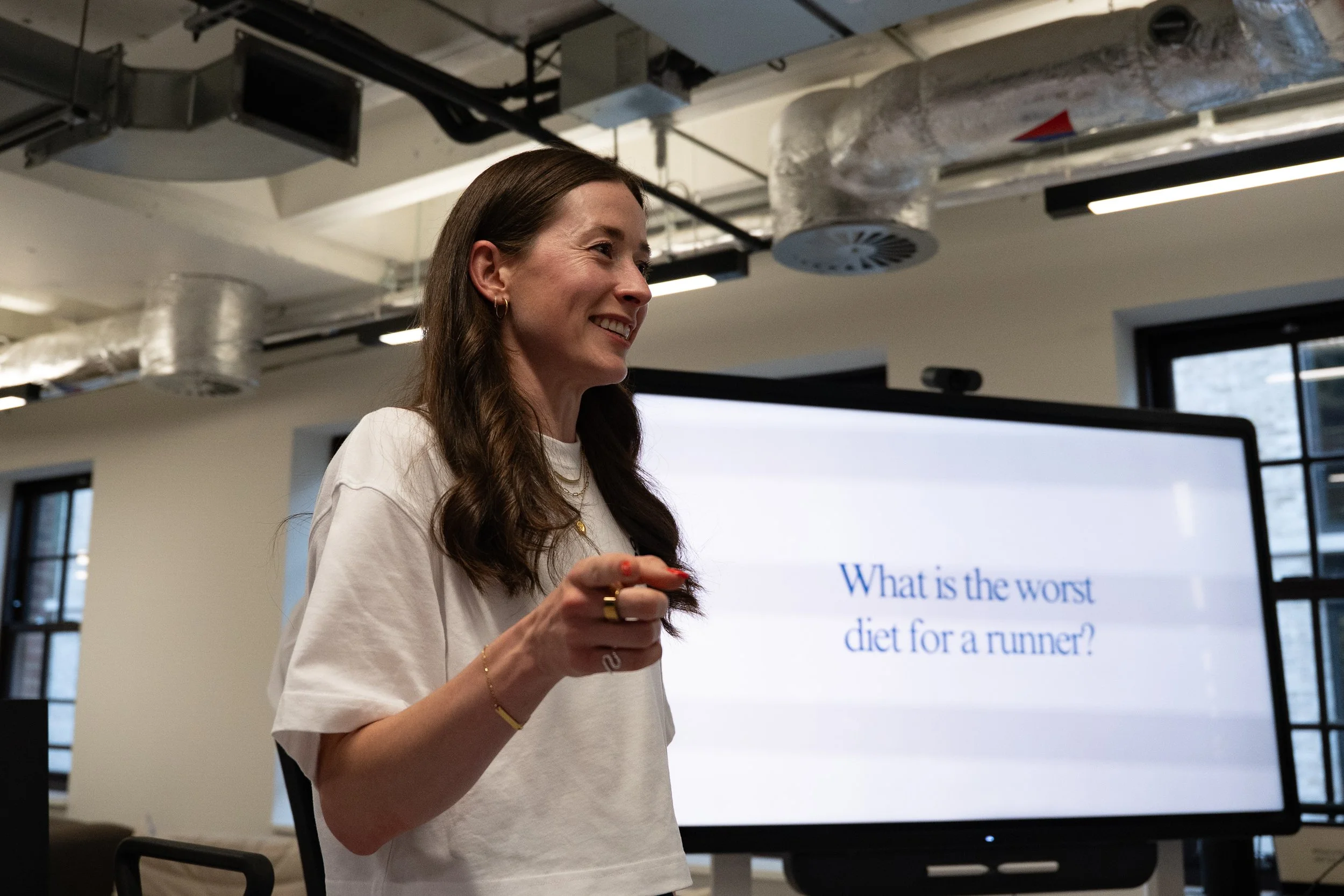 A woman presenting in a conference room with a screen behind her displaying a question about the worst diet for a runner.