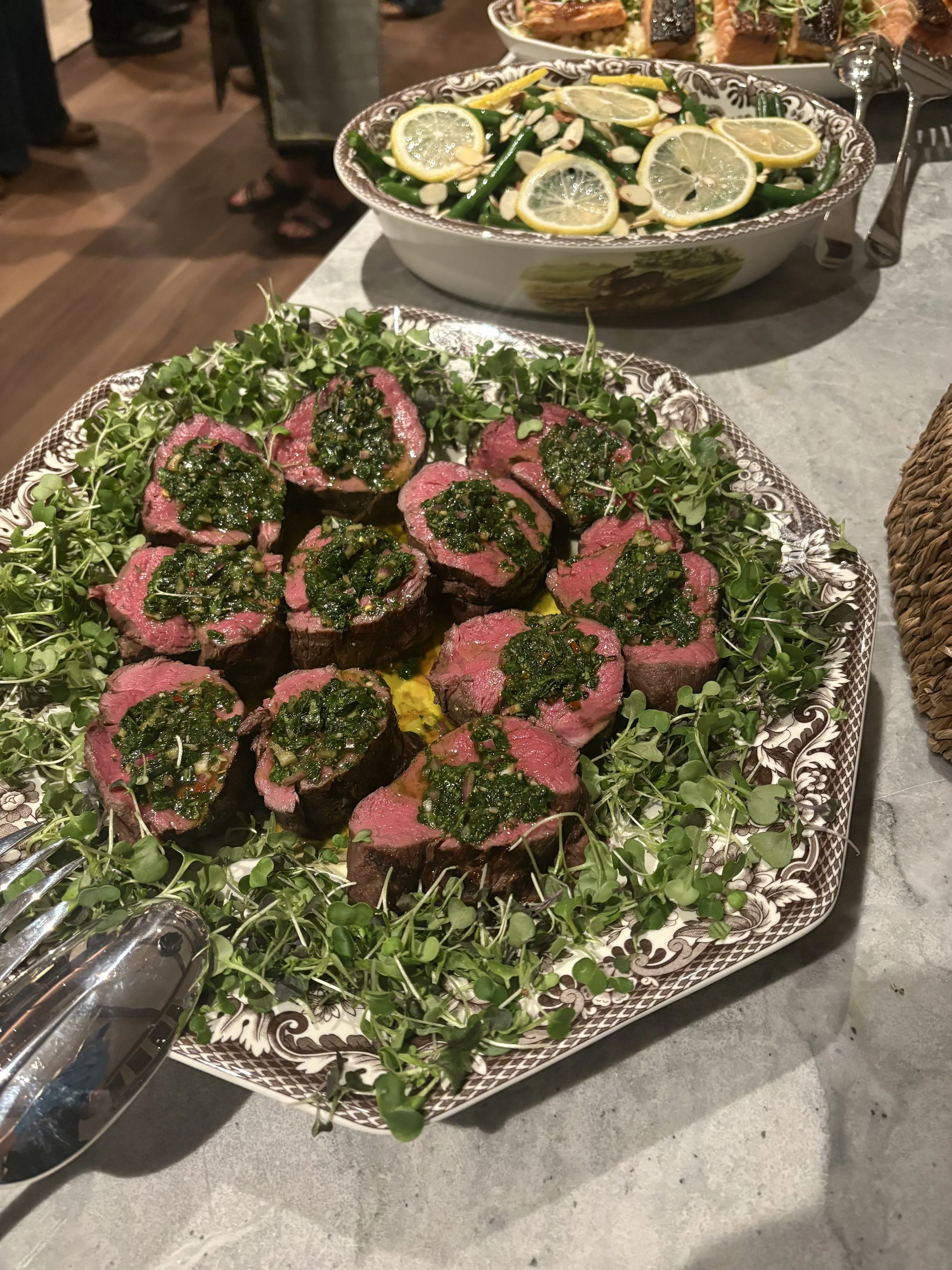 Plate of sliced rare steak topped with green herb sauce, garnished with microgreens, on a decorative platter.