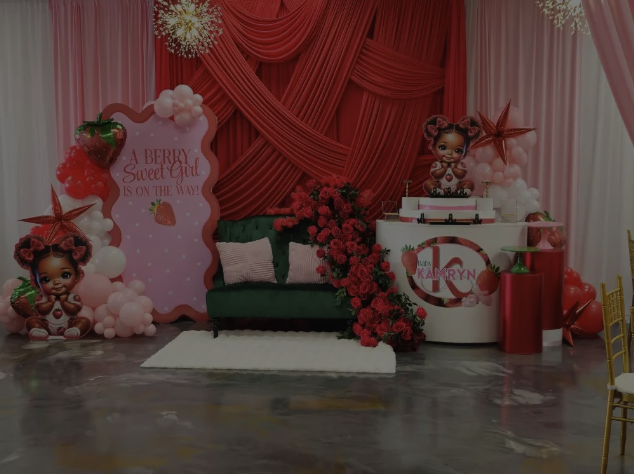 Party backdrop with pink drapes, balloons, and stuffed animal characters, including a teal couch adorned with pink flowers and a cake table with an ice cream themed logo.