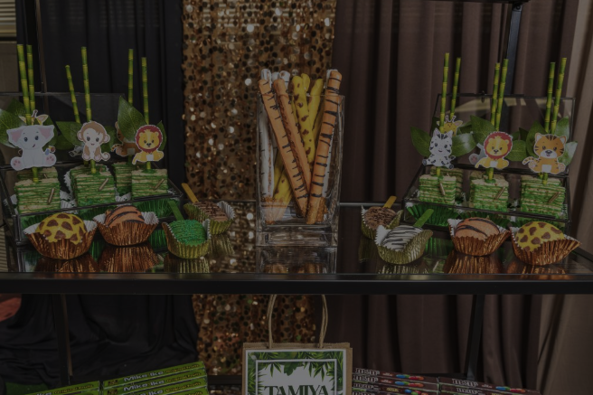 Party dessert table with animal-themed cupcakes and treats, decorated with green and animal figures, and bamboo-themed straws in the background