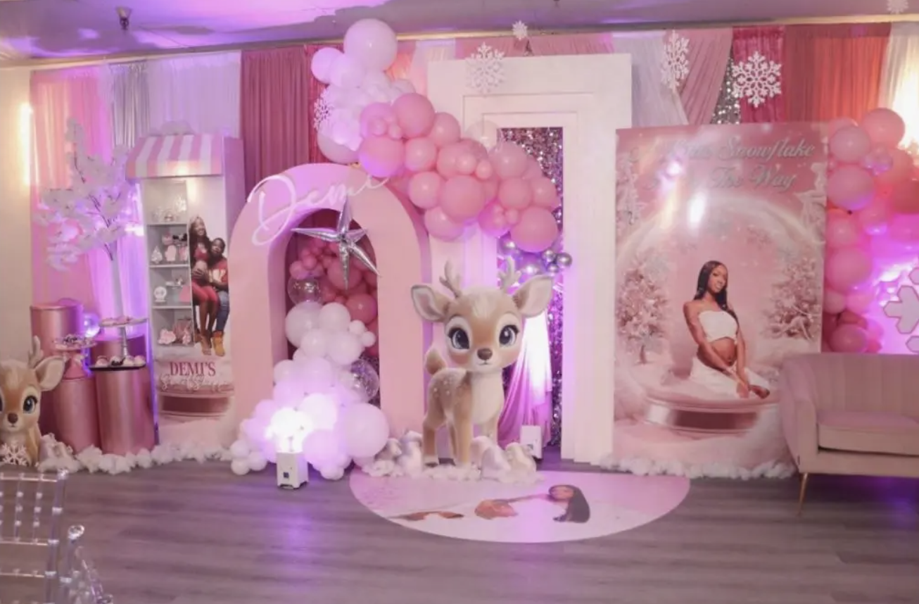 Decorations for a young girl's birthday party with pink and white balloons, a large Reindeer character, a backdrop with a girl in a white dress sitting on snow, and pink curtains.