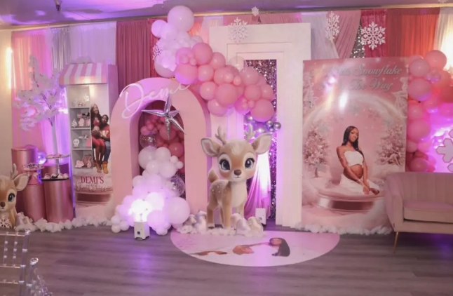 Decorated indoor space for a celebration with pink and white balloons, a large plush deer figure, a backdrop with a girl sitting on a swing, and a pink-themed princess setup.