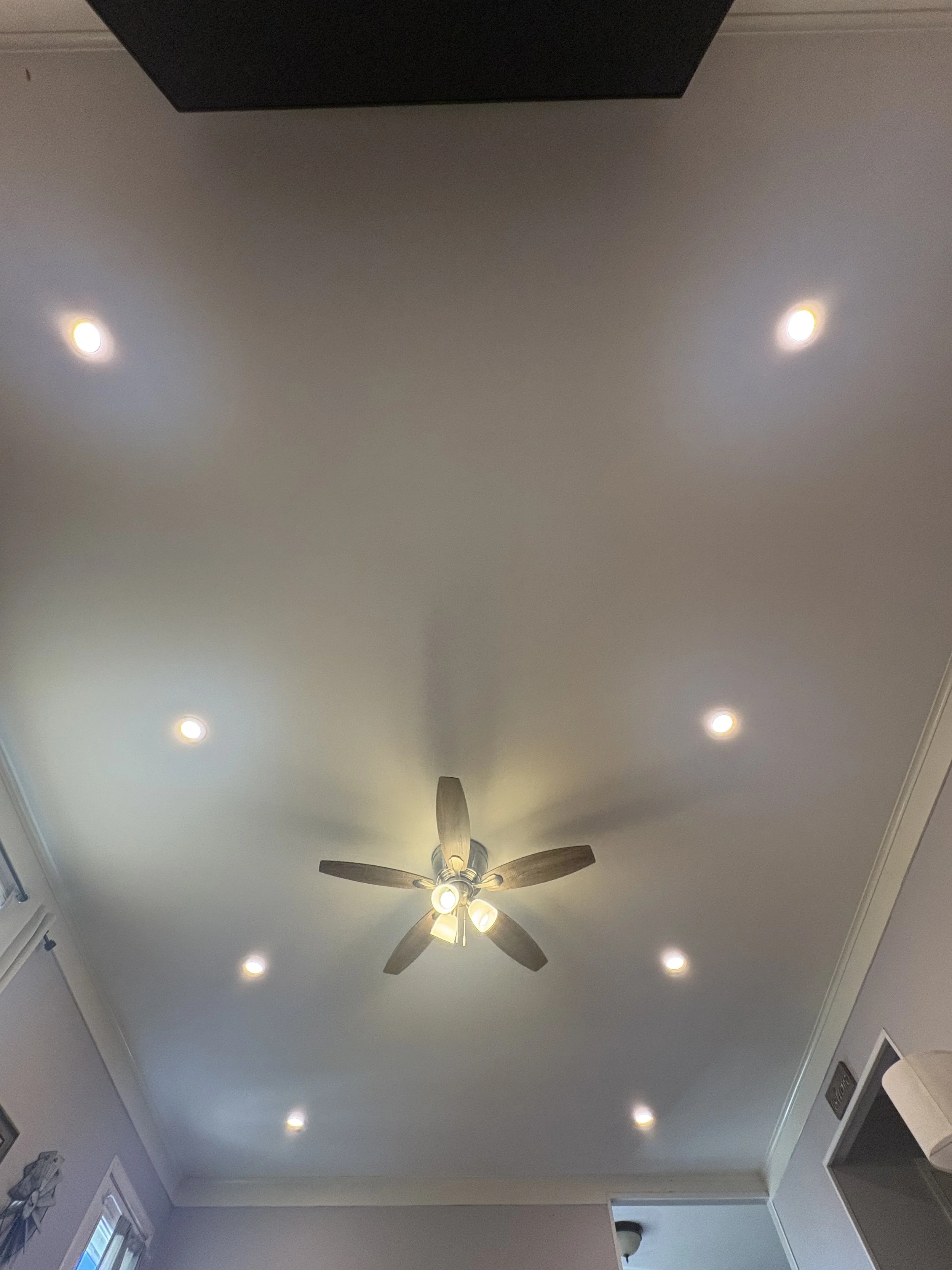 Ceiling with eight LED lights, a ceiling fan with five wooden blades and four light bulbs, and part of the walls and windows.