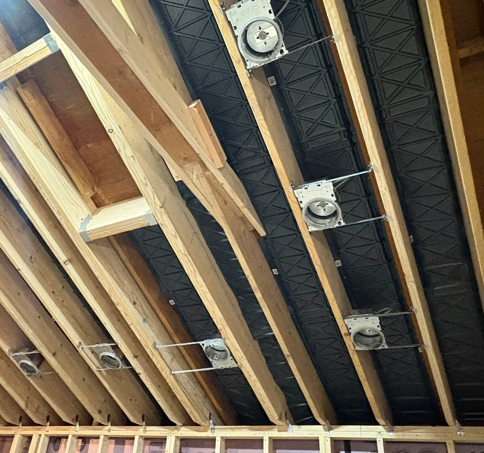 Ceiling framework with wooden beams, black air ducts or pipes, and silver circular vents in a building under construction.