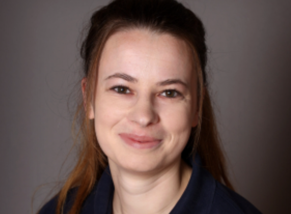 Portrait of a woman with brown hair smiling against a neutral gray background.