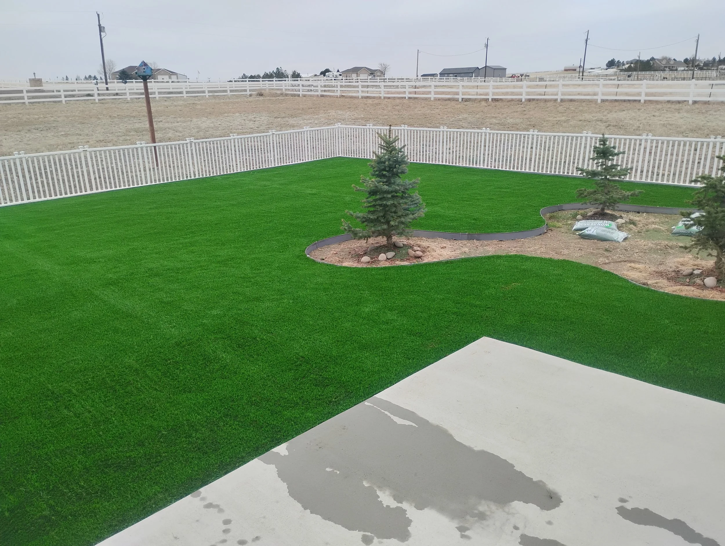 Artificial turf installed on a large lawn, around a rock-bed with original trees in it.