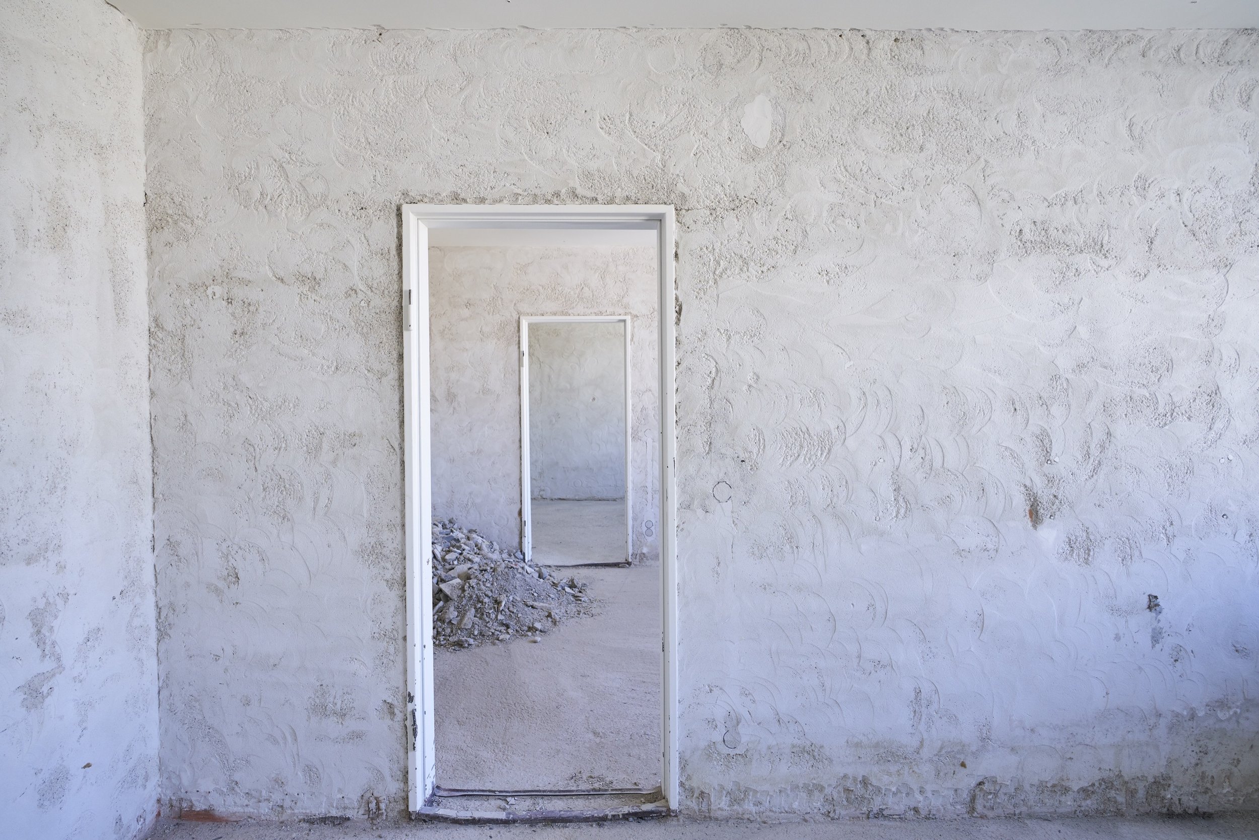 Leere weiße Wand und mehrere offene Türen in einem Gebäude, durch die weitere Räume sichtbar sind,  während Abrissarbeiten der Firma Ettengruber GmbH.
