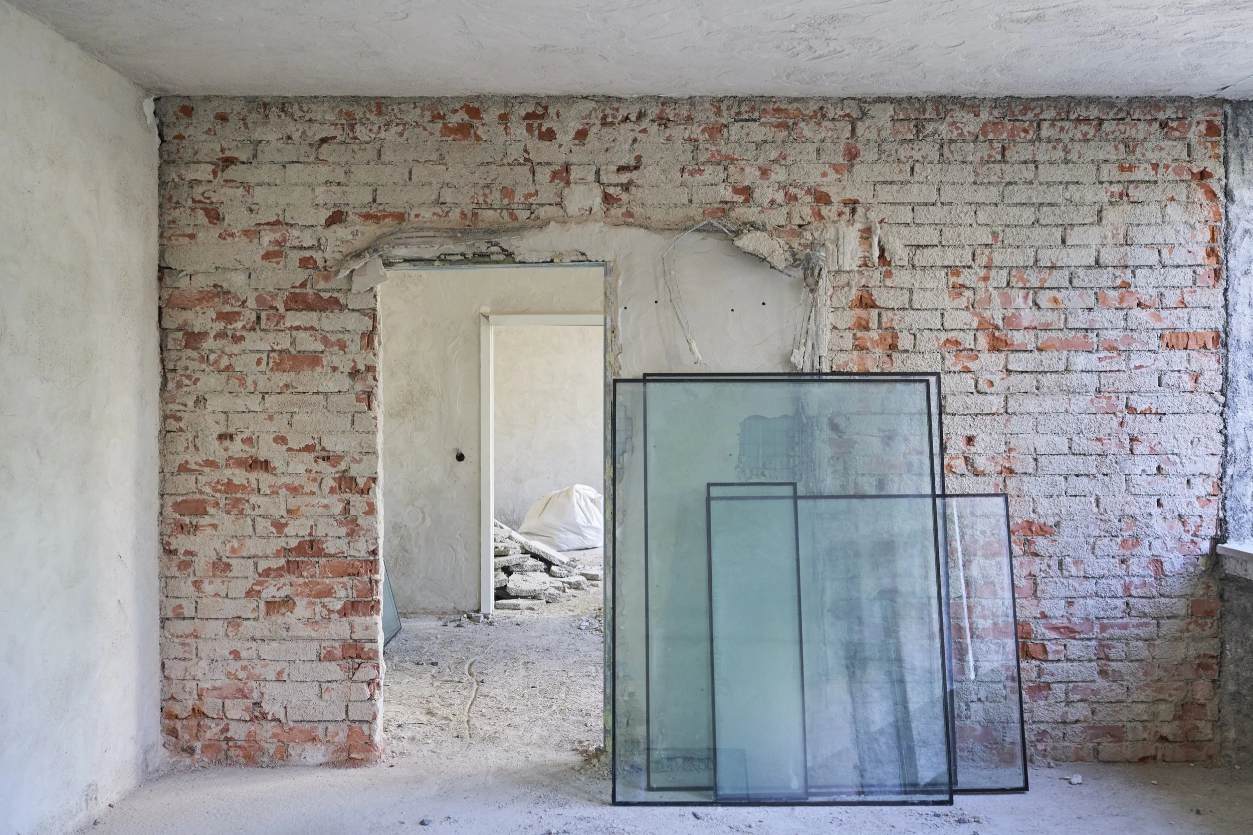 Innenraum eines Zimmers während der Abrissarbeiten mit einer offenen Tür und drei Glasplatten vor einer unvollständigen Ziegelwand. Abrissarbeiten der Firma Ettengruber GmbH.
