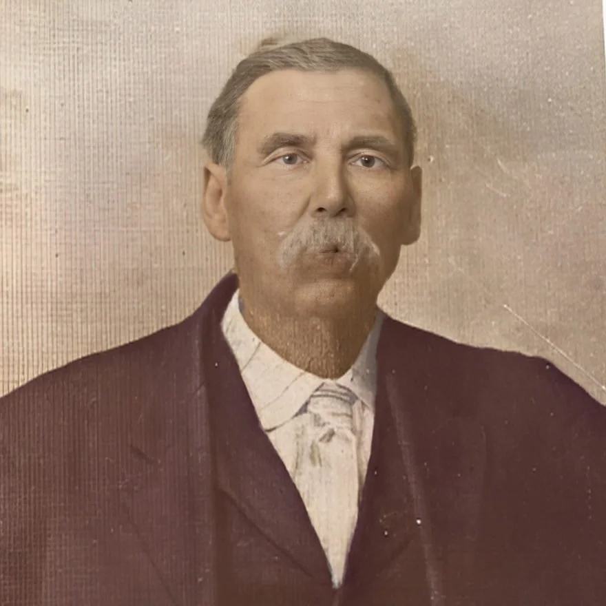 A vintage portrait of a middle-aged man with a mustache, wearing a dark jacket and a light-colored collared shirt, against a plain background.