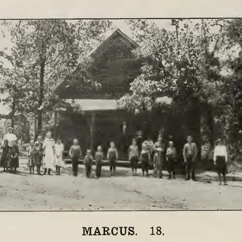 Historical black and white photograph of a group of children and an adult standing in front of a house with trees in the background.