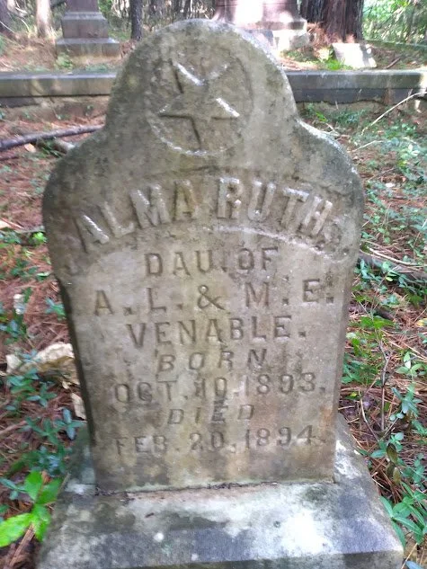 Old gravestone for A. M. Ruth, daughter of A. L. and M. E. Venable, born October 19, 1893, died February 20, 1894, in a cemetery surrounded by trees.