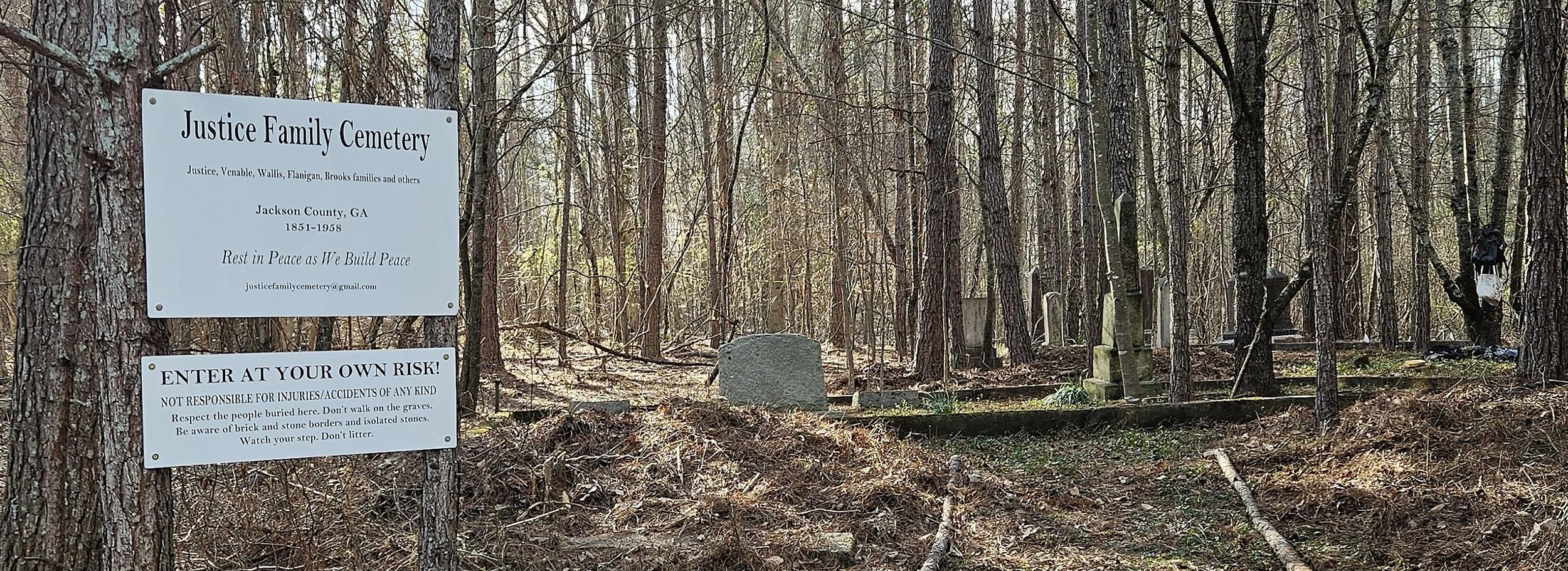 Sign on a tree at Justice Family Cemetery in Jackson County, Georgia, with historical information and a warning to visitors, surrounded by trees and gravestones.