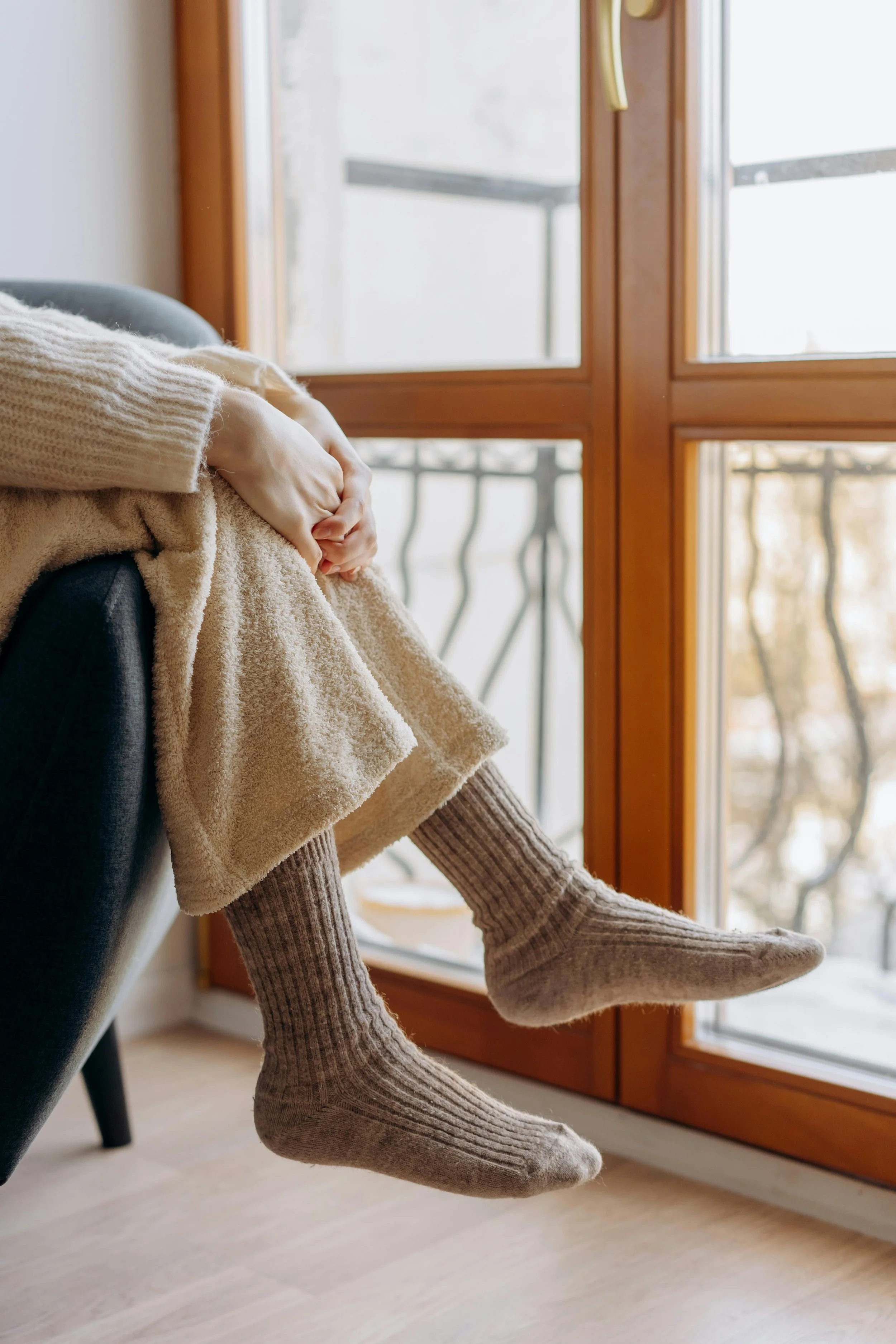 Person in cozy clothing looking out a window, symbolizing contemplation and transition