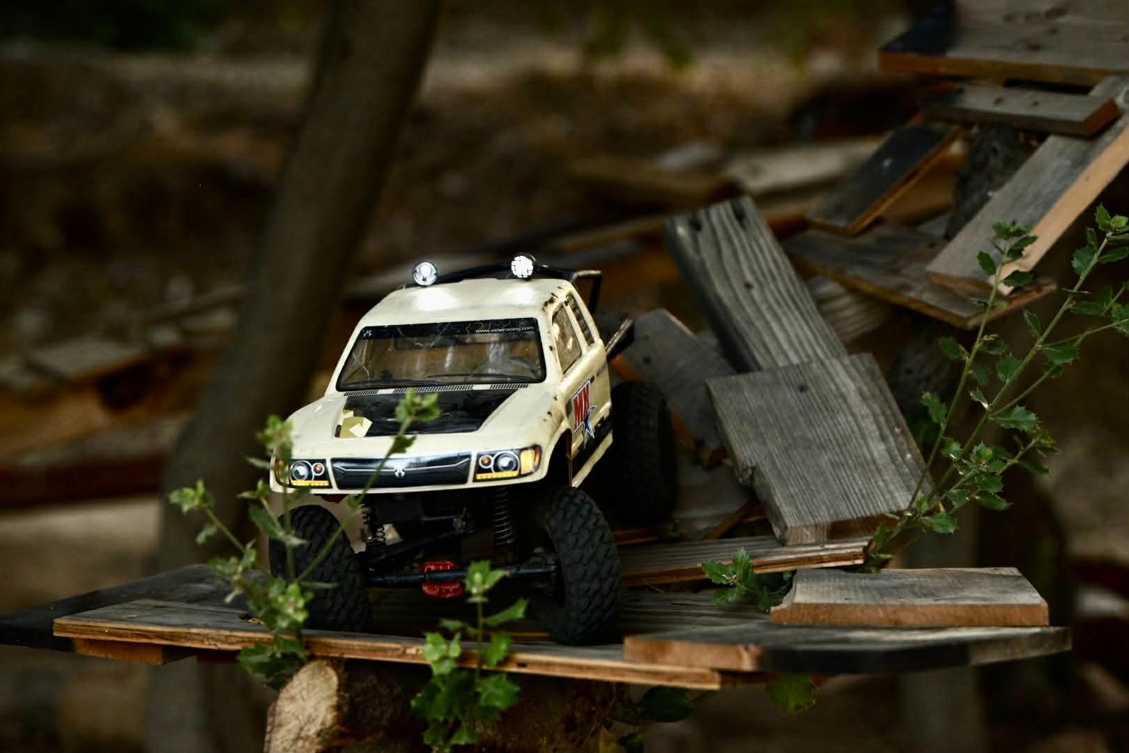 A miniature white off-road toy vehicle on a weathered wooden platform outdoors.