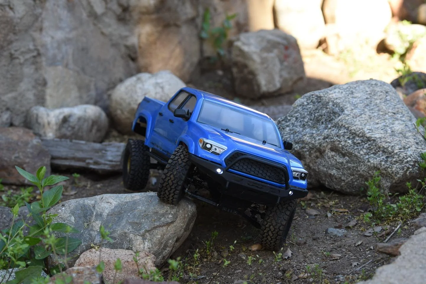 A blue remote control toy truck navigating over rocks and uneven terrain outdoors.