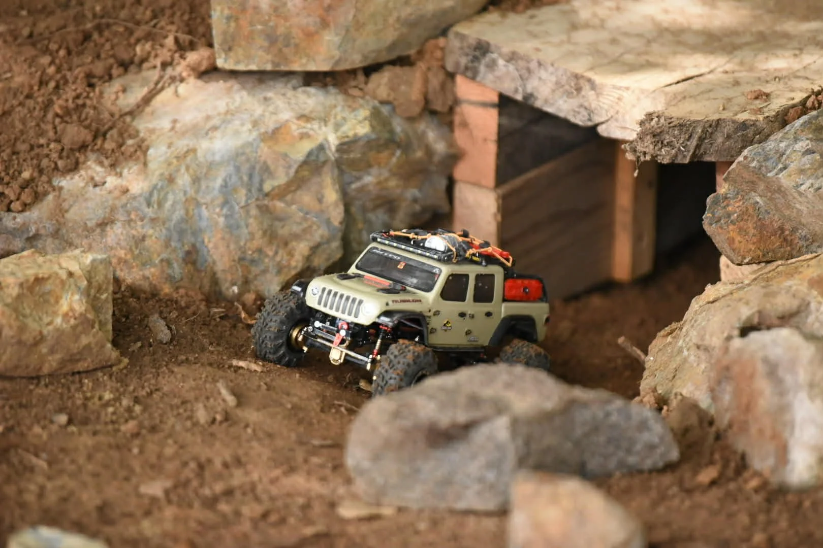 Miniature off-road vehicle navigating through rocky terrain with a small tunnel in the background.
