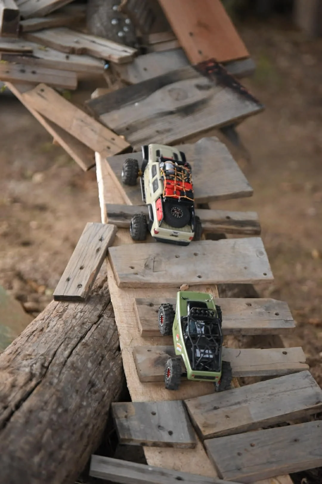 Two toy off-road trucks climbing a homemade wooden ramp outdoors