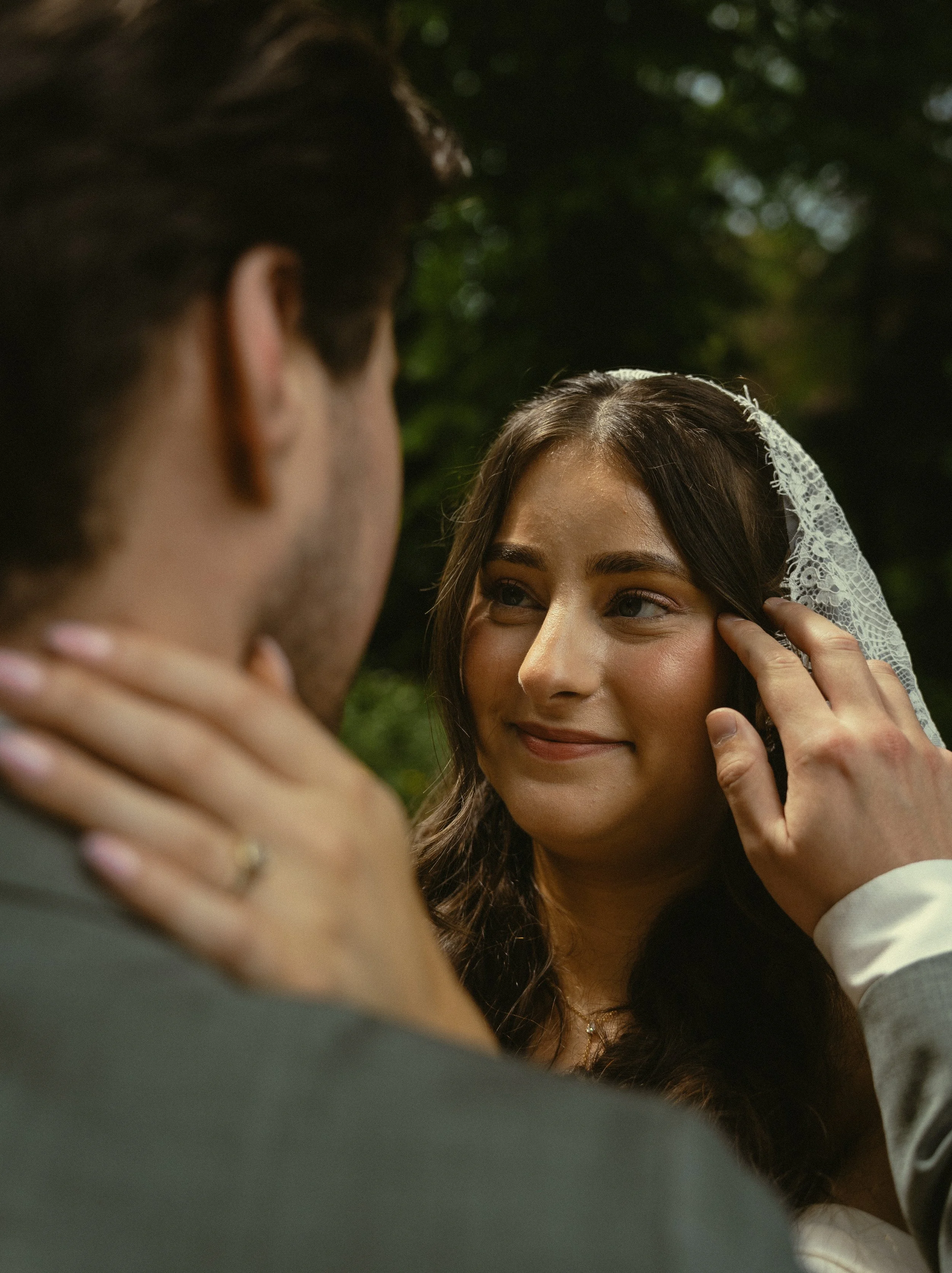 Een close-up van een stel tijdens een huwelijk, de vrouw kijkt liefdevol naar de man terwijl hij haar hand aanraakt.