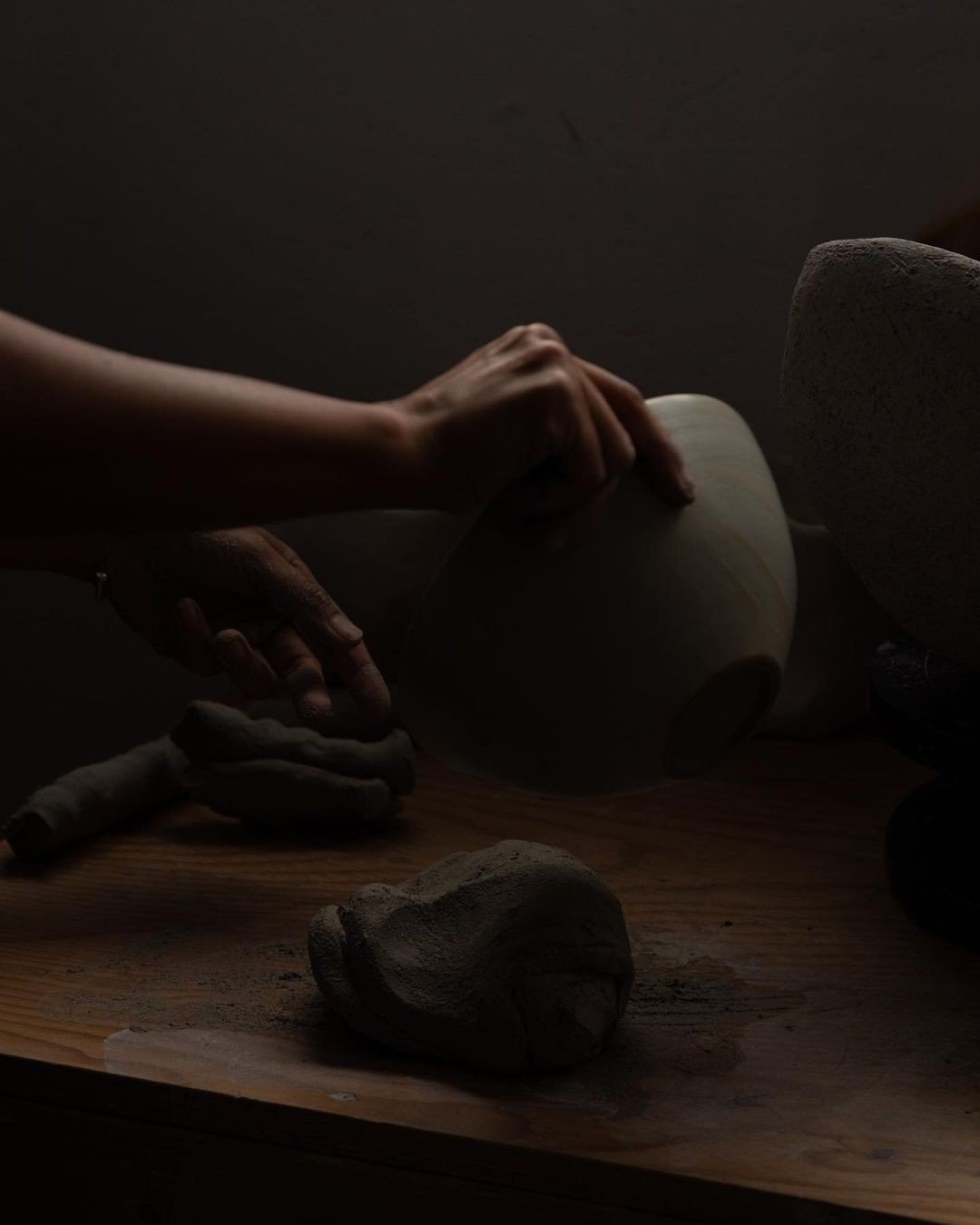 Hands shaping clay on a pottery wheel in a dimly lit setting.