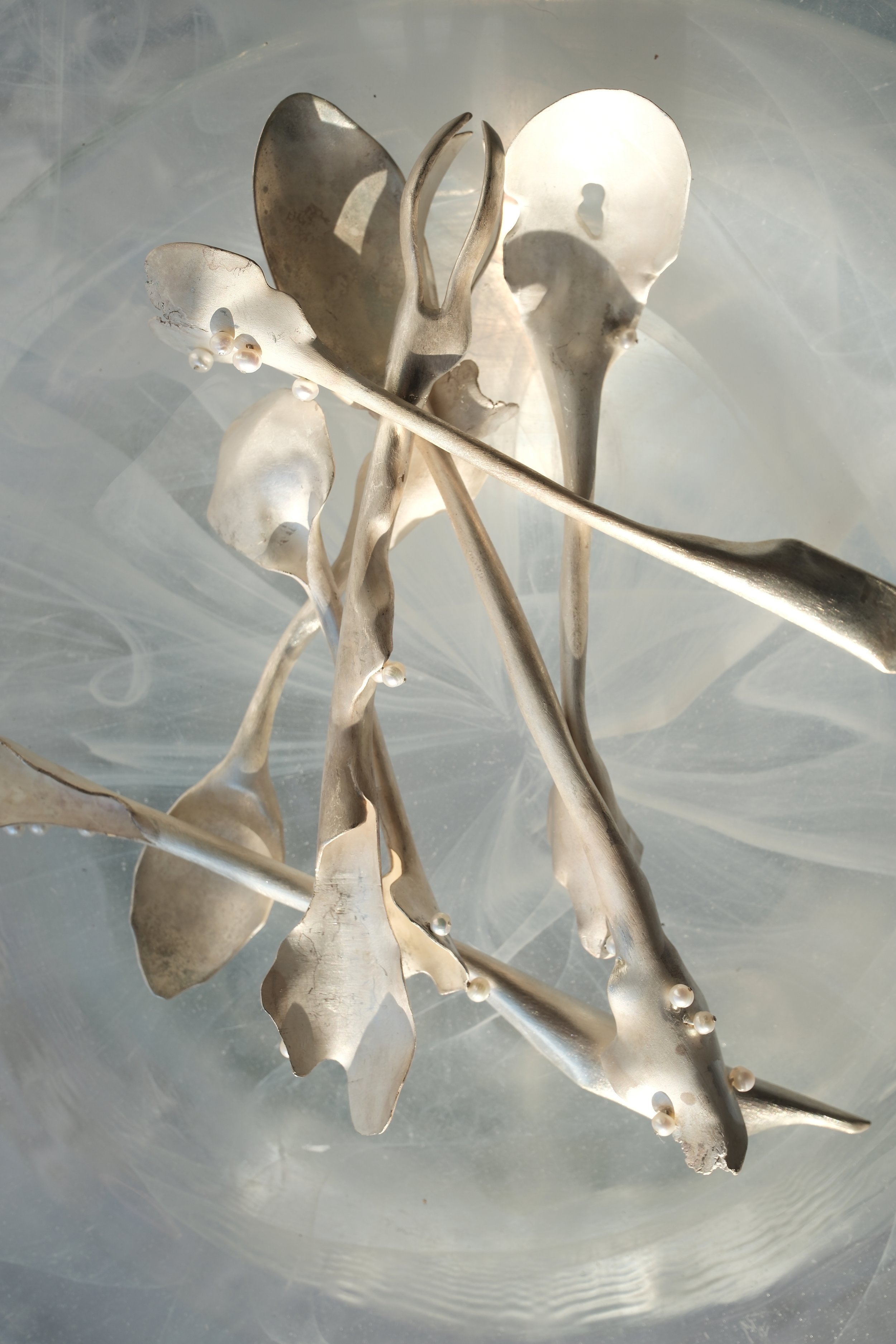 Silver abstract sculpture with curved and flowing shapes, set against a reflective surface.