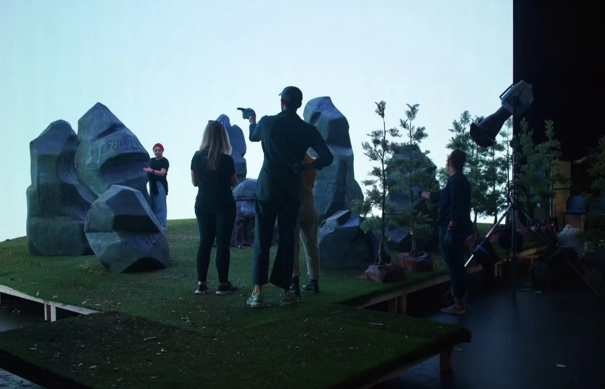 People preparing a set in a studio with artificial trees and large rocks for a production.