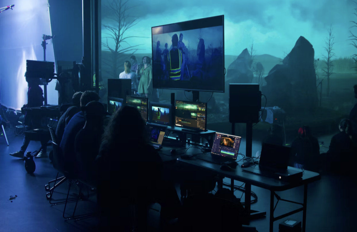 People working on video production or editing in a studio with monitors, large screen, and scenic background.