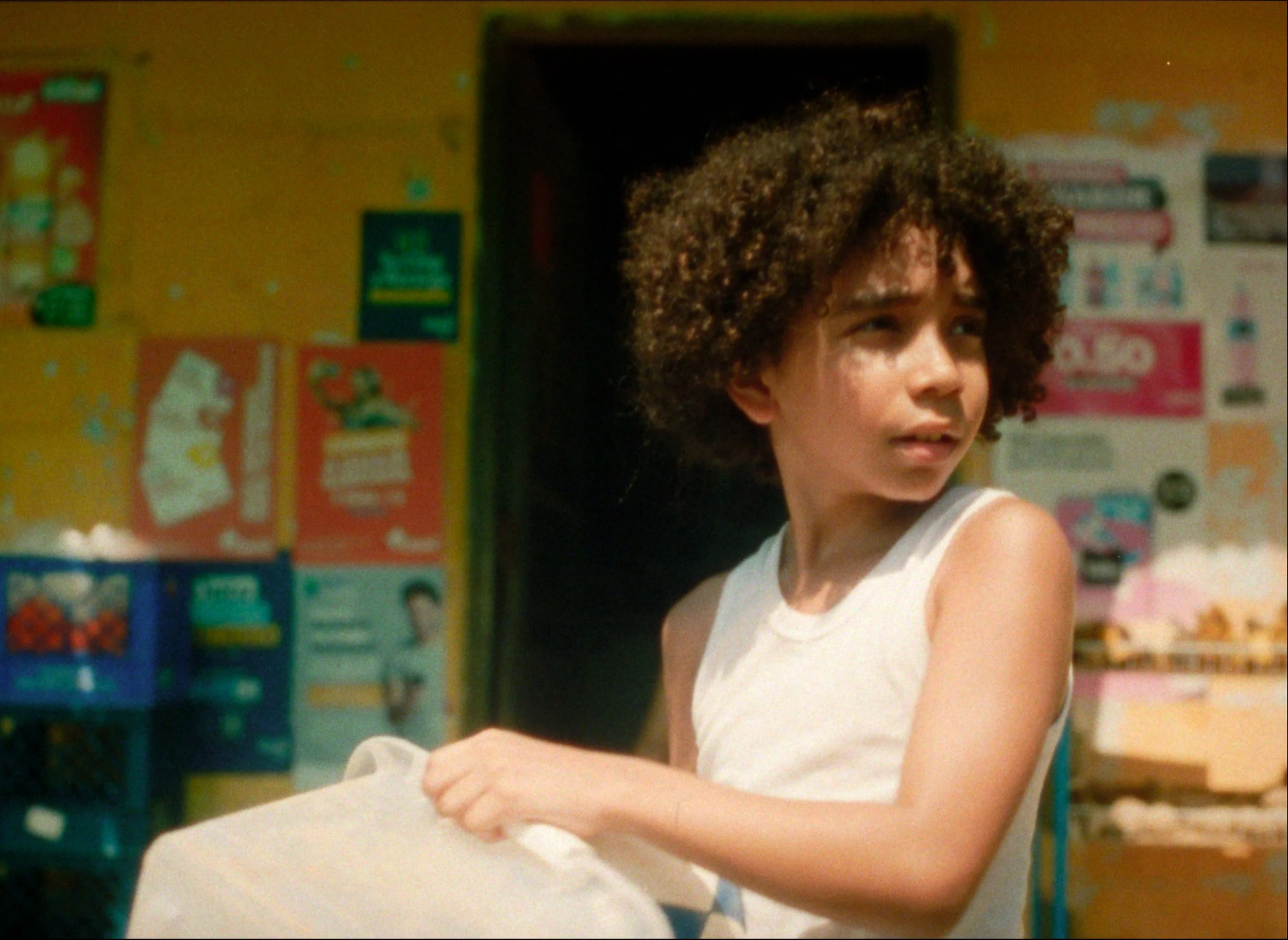 A young girl with curly hair in a white sleeveless top in a colorful store or shop.