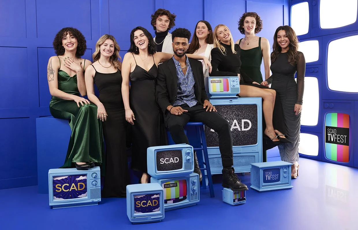 Group of eight young people in formal attire posing with vintage TV sets in a bright blue studio with TV festival branding.