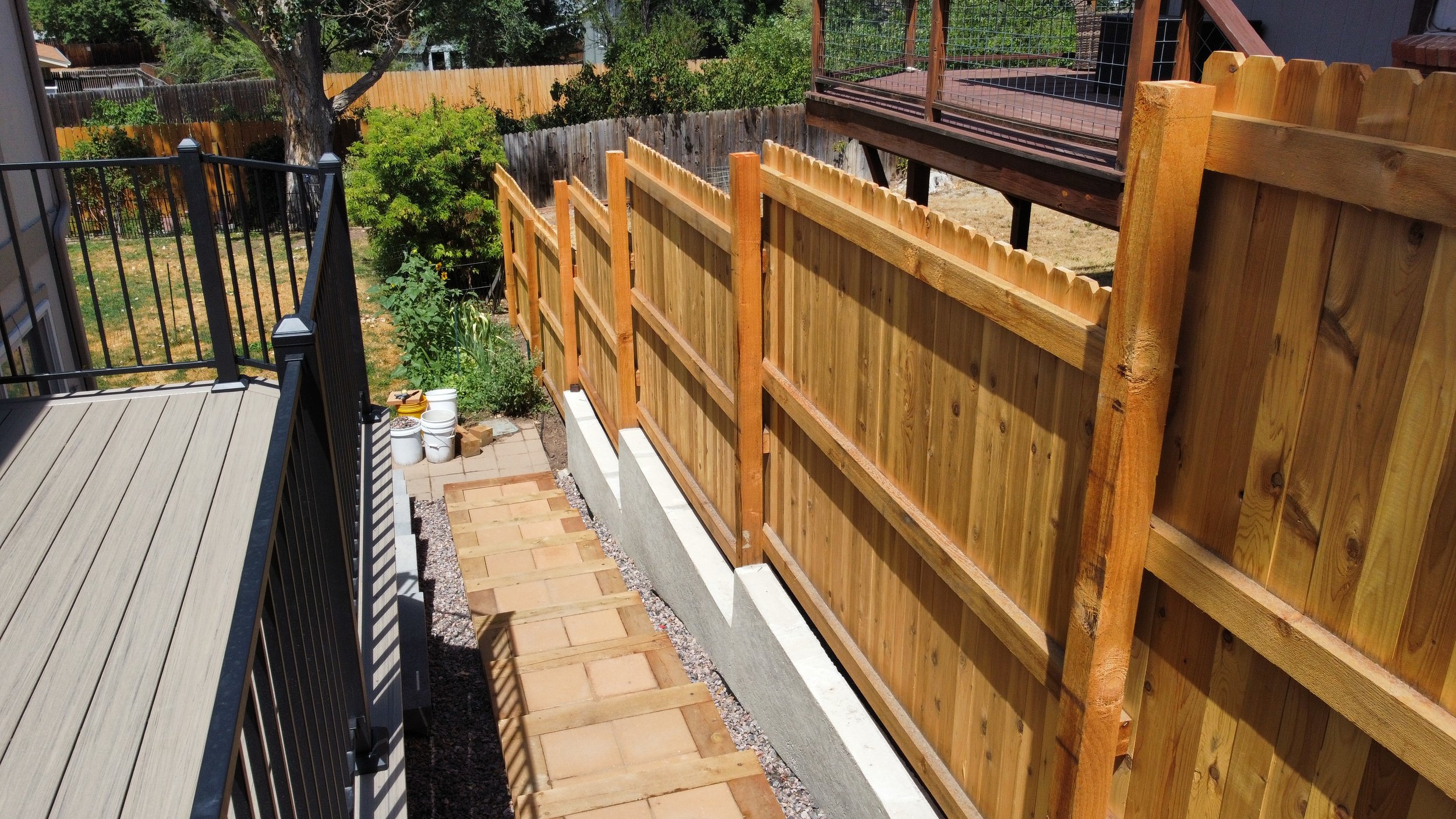 Backyard with a wooden privacy fence, new fence panels, paved stepping stones, and a small garden area with plants and buckets. Mile High Decks Specializing in Decks and Outdoor living space. Deck Builder Specialist in Douglass County Colorado, 