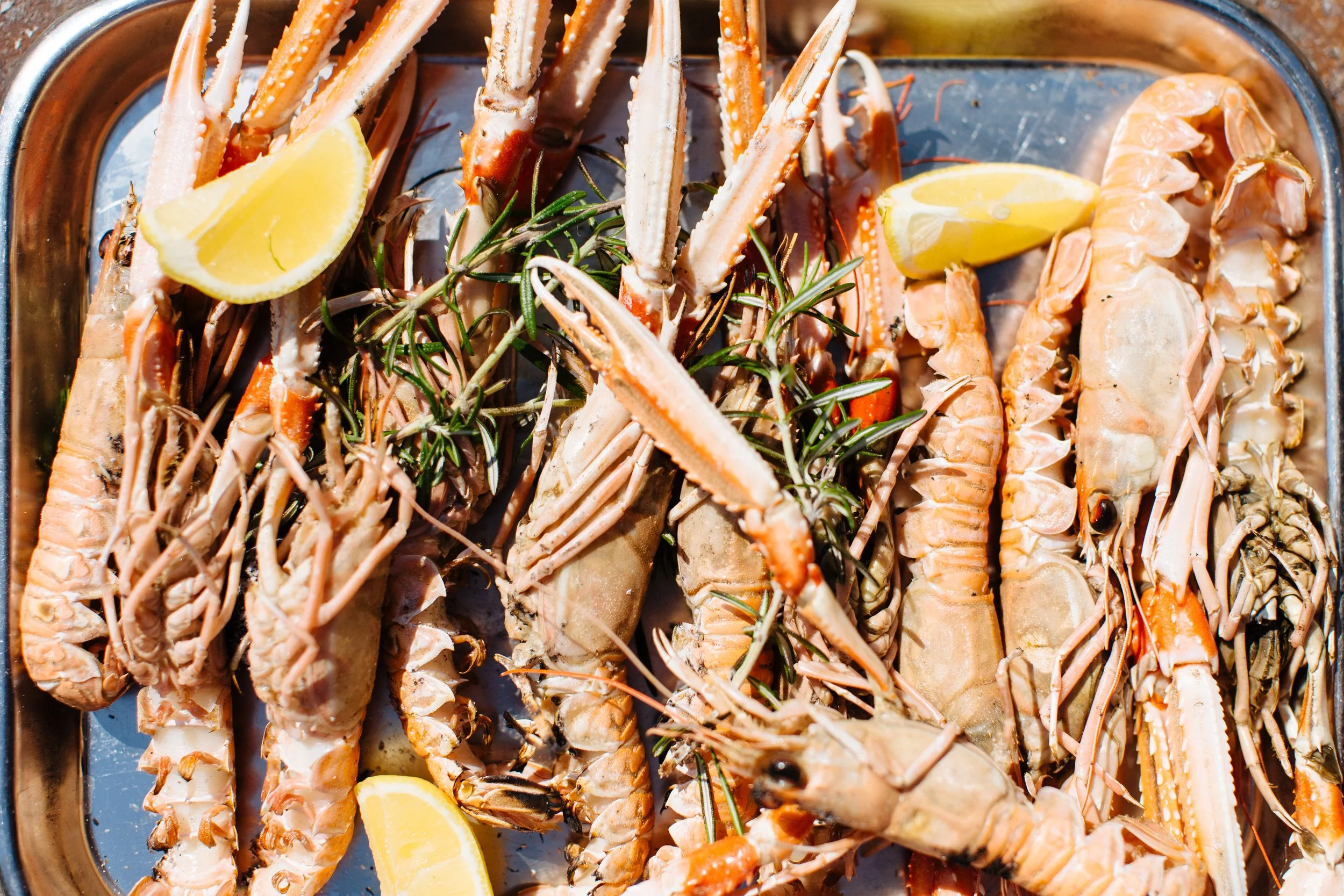 A tray of cooked lobster tails garnished with lemon wedges and sprigs of rosemary.