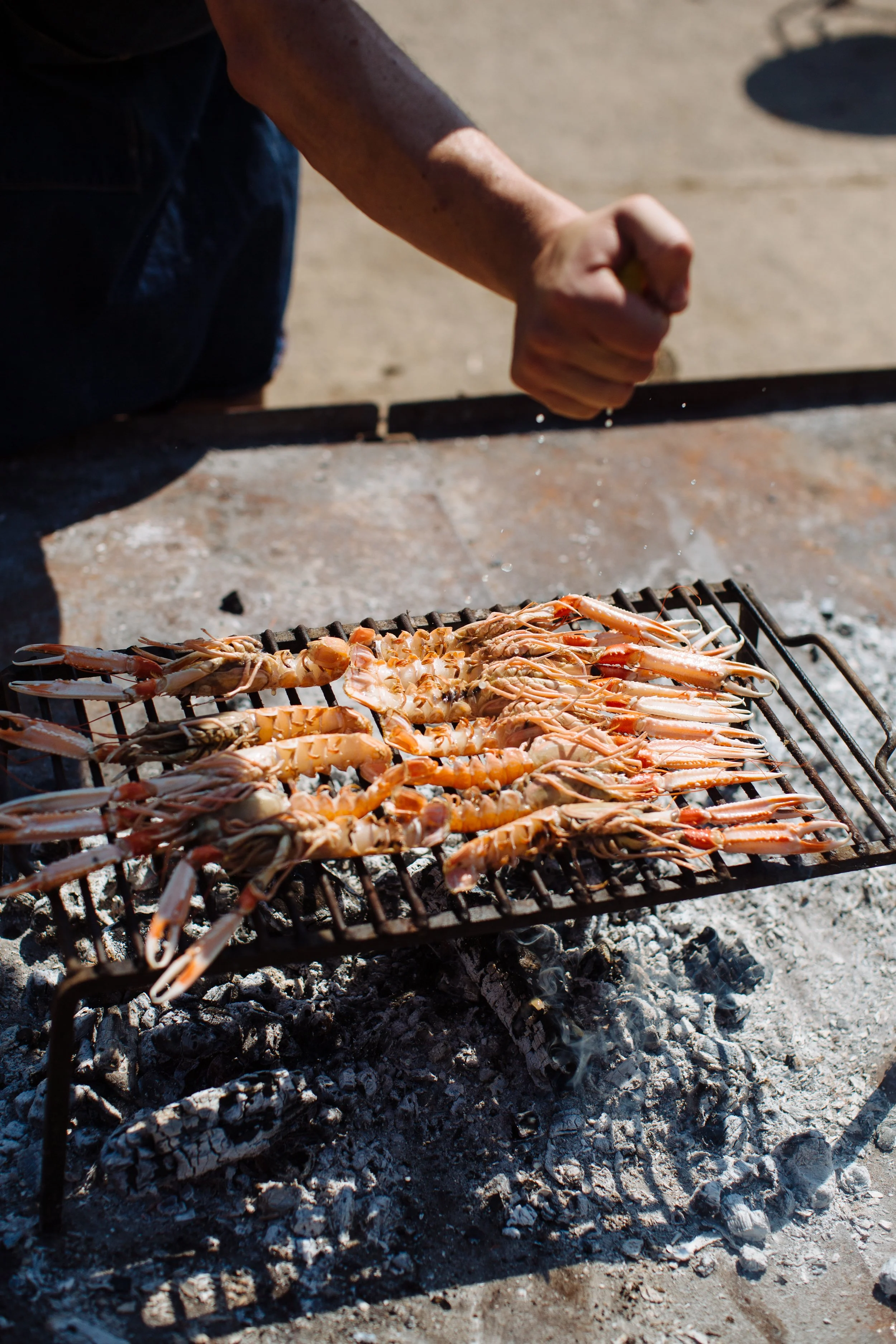 Person grilling lobster tails over an open fire on a metal grill outdoors.