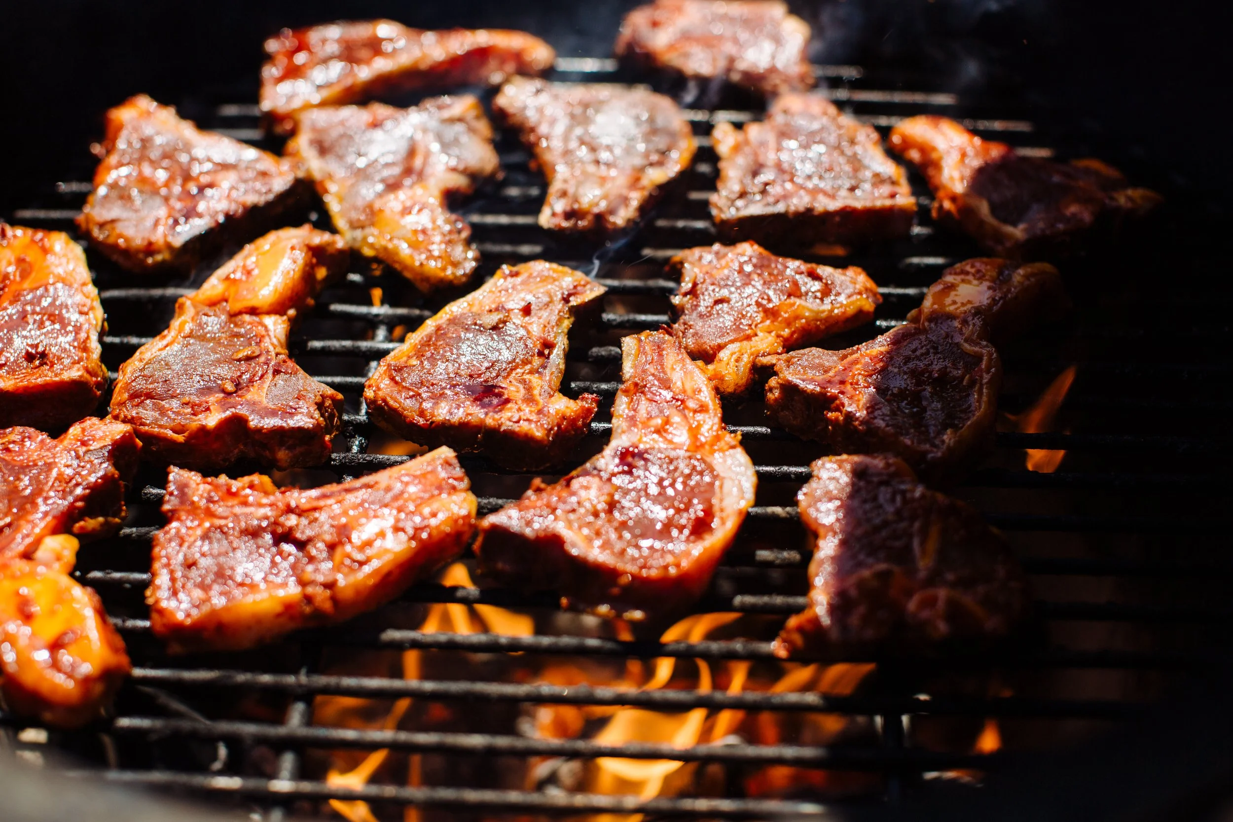 Beef steaks cooking on a grill over open flames.