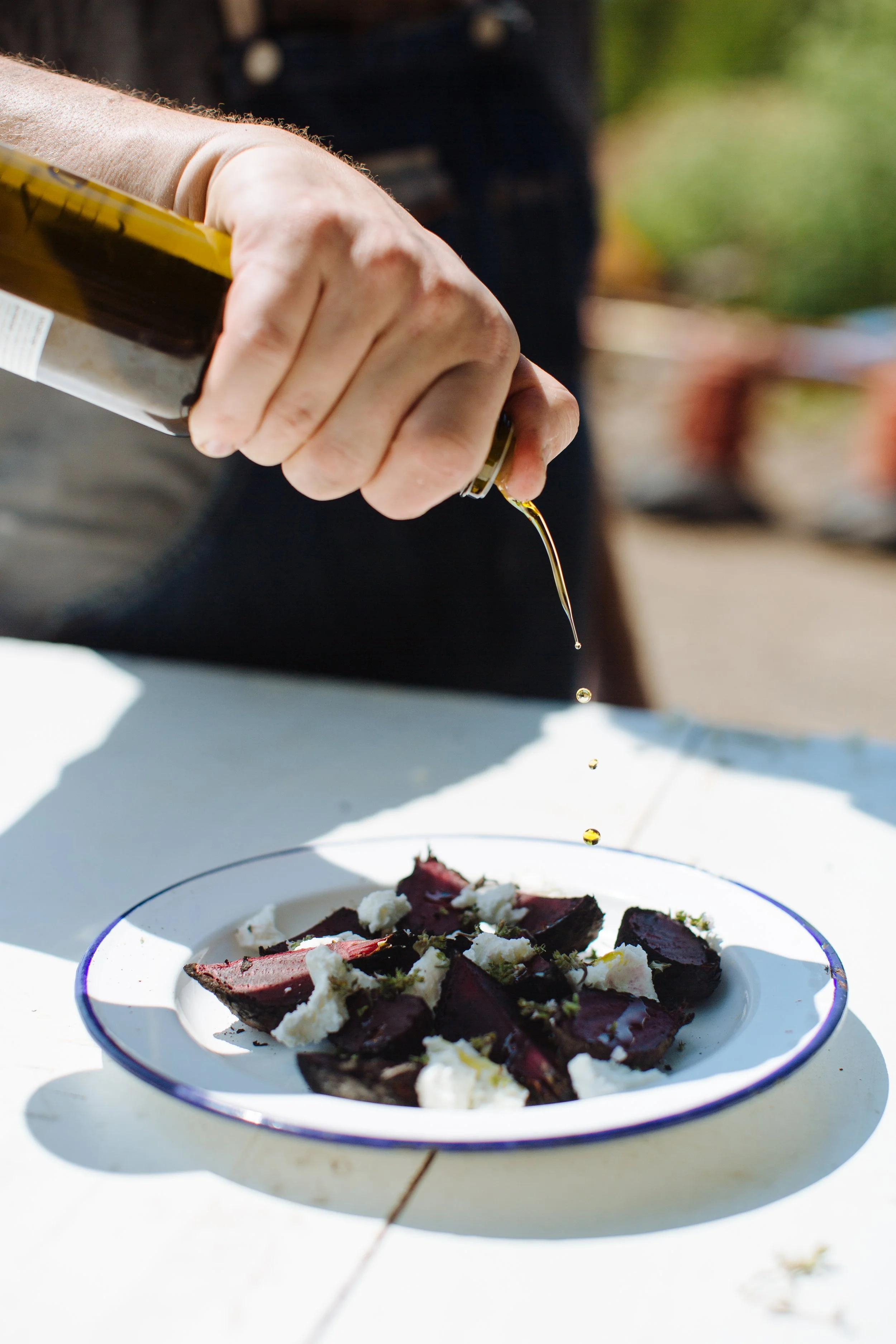 Person pouring oil over a dish with slices of beet and cheese.