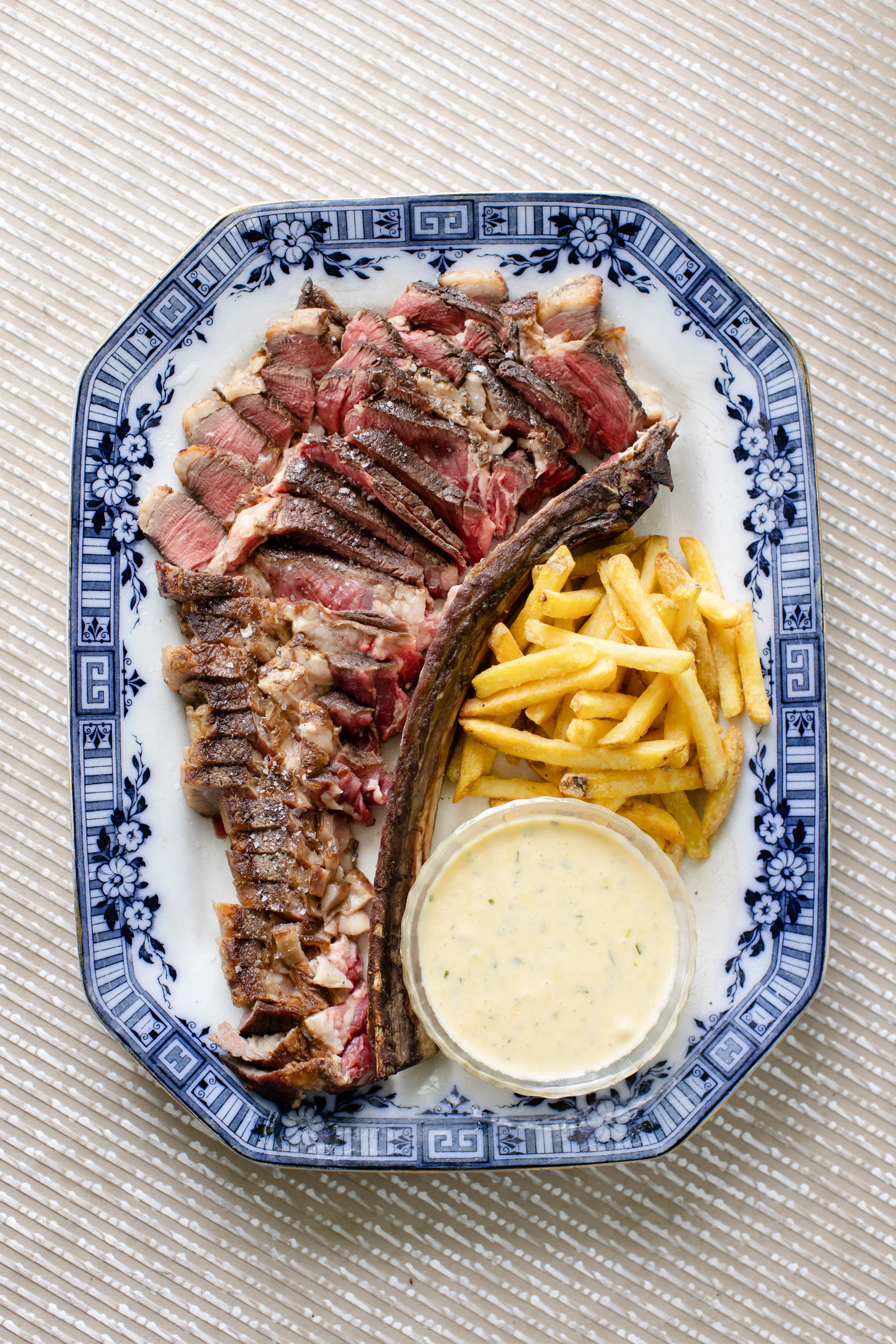 Plate with sliced steak, French fries, a jalapeño, and dipping sauce on a patterned plate.