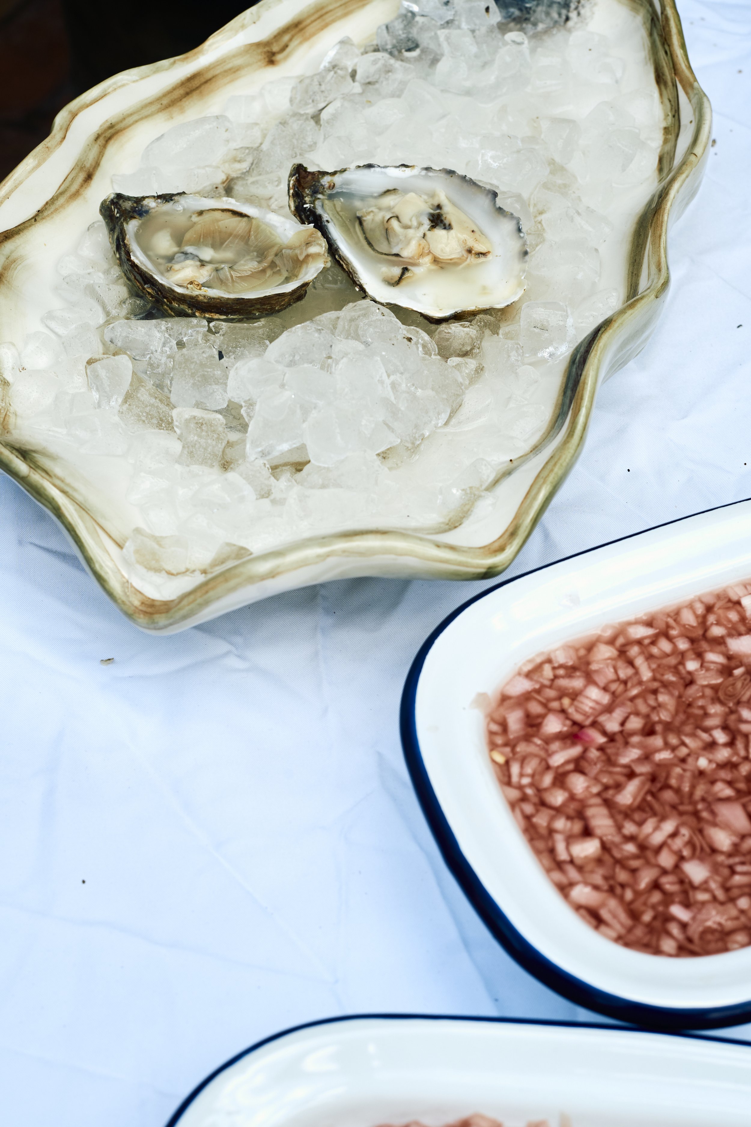 Fresh oysters on ice in a decorative bowl and a bowl of chopped red onions.