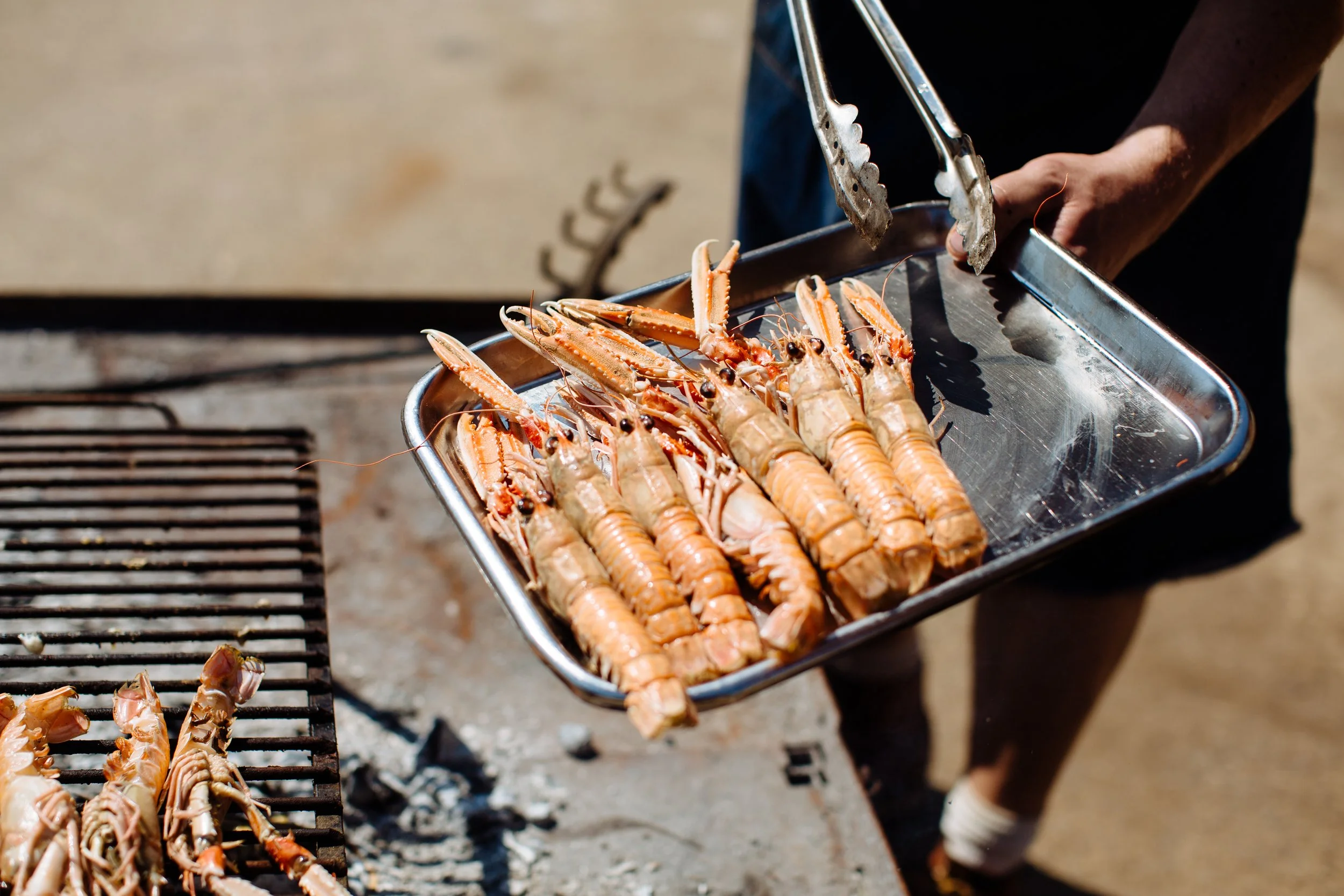Person grilling lobster tails on a barbecue grill outdoors.