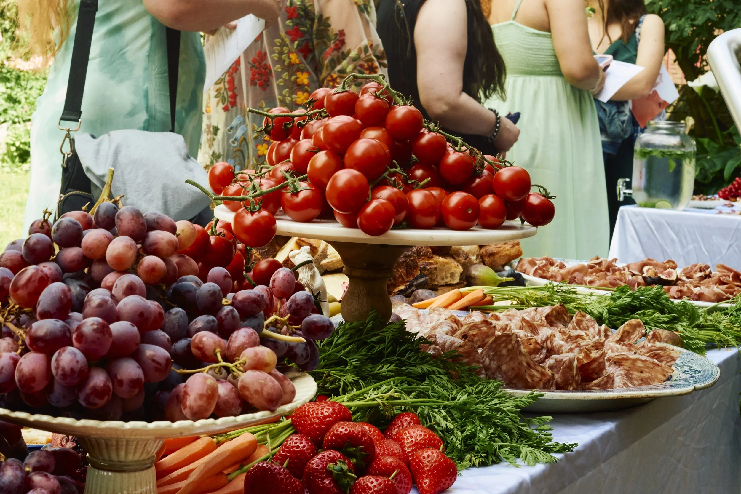 Table with fresh grapes, strawberries, cherries, and vegetables at an outdoor gathering