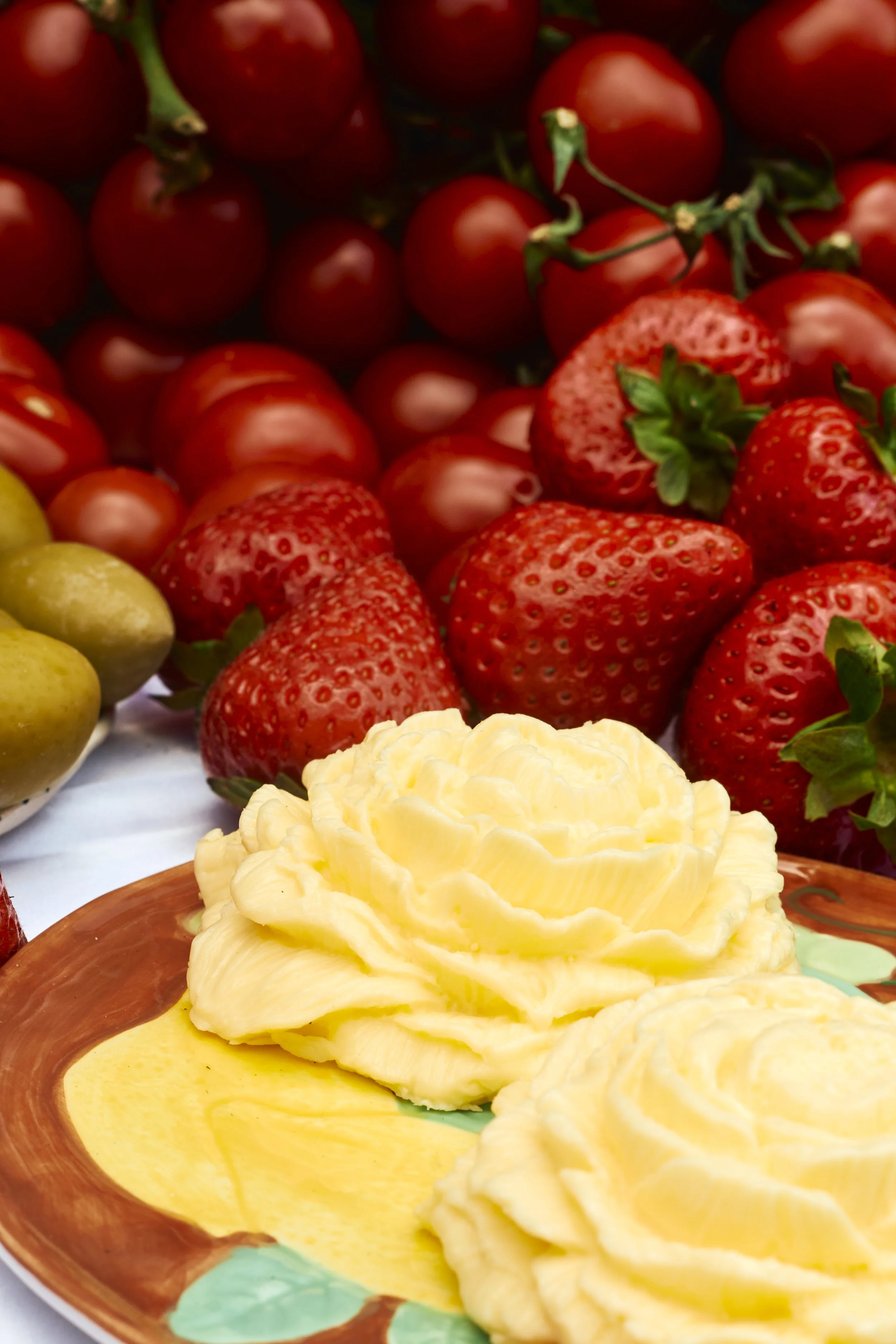 A plate of butter served with fresh strawberries, grapes, and cherry tomatoes.