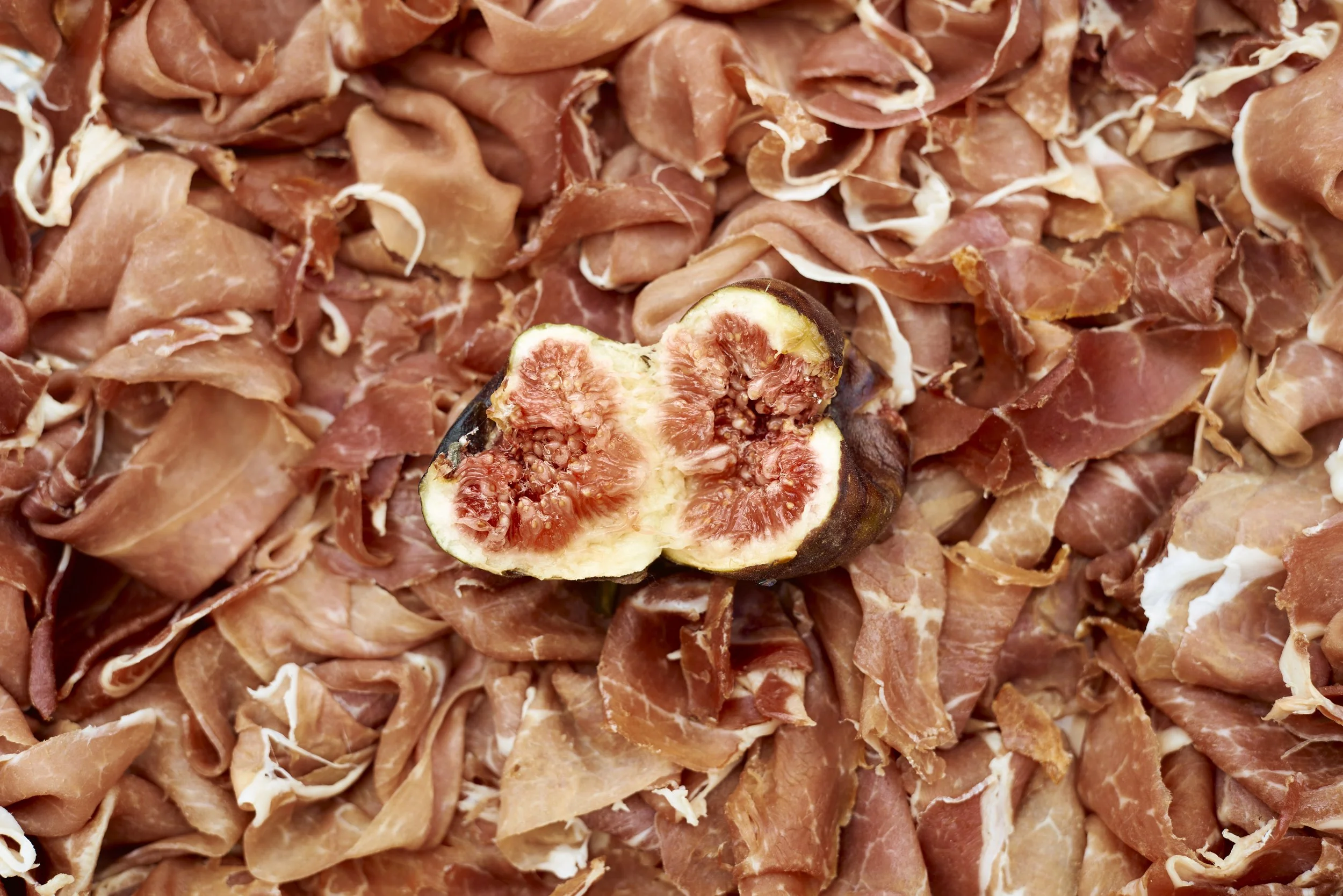 A fresh fig cut in half on a bed of thinly sliced prosciutto.