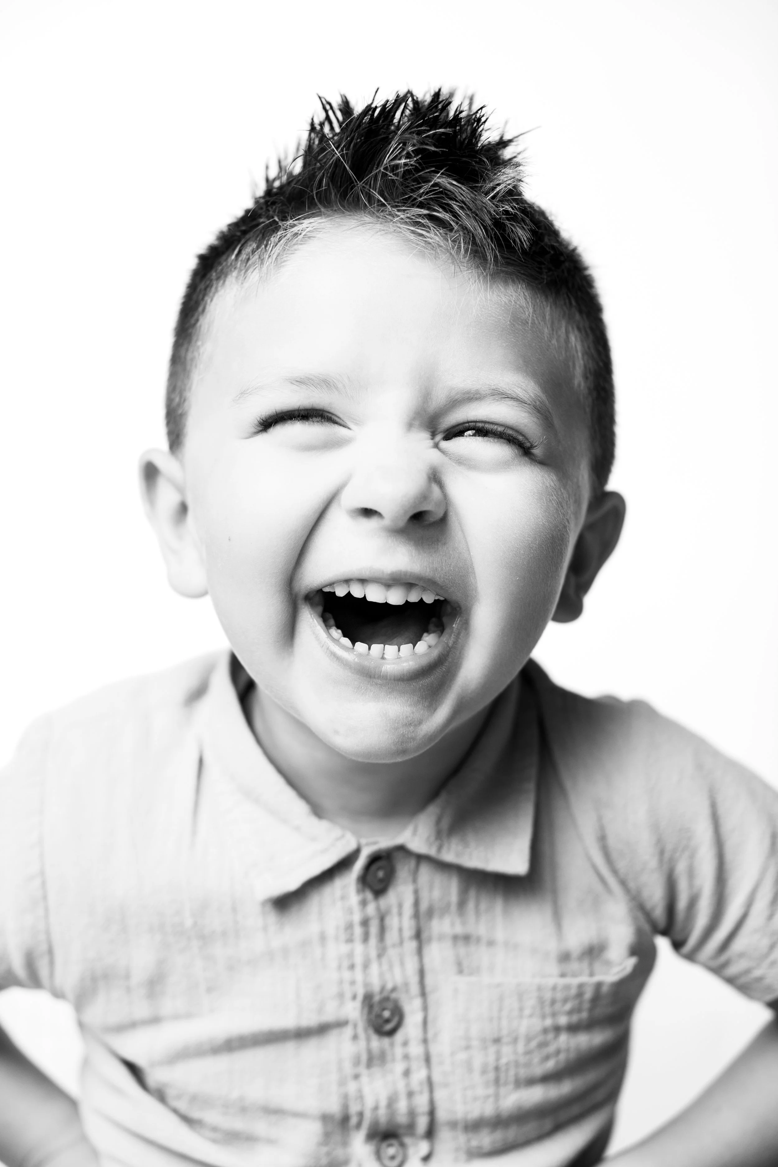 A young boy with spiky hair laughing joyfully, wearing a collared shirt, in black and white.