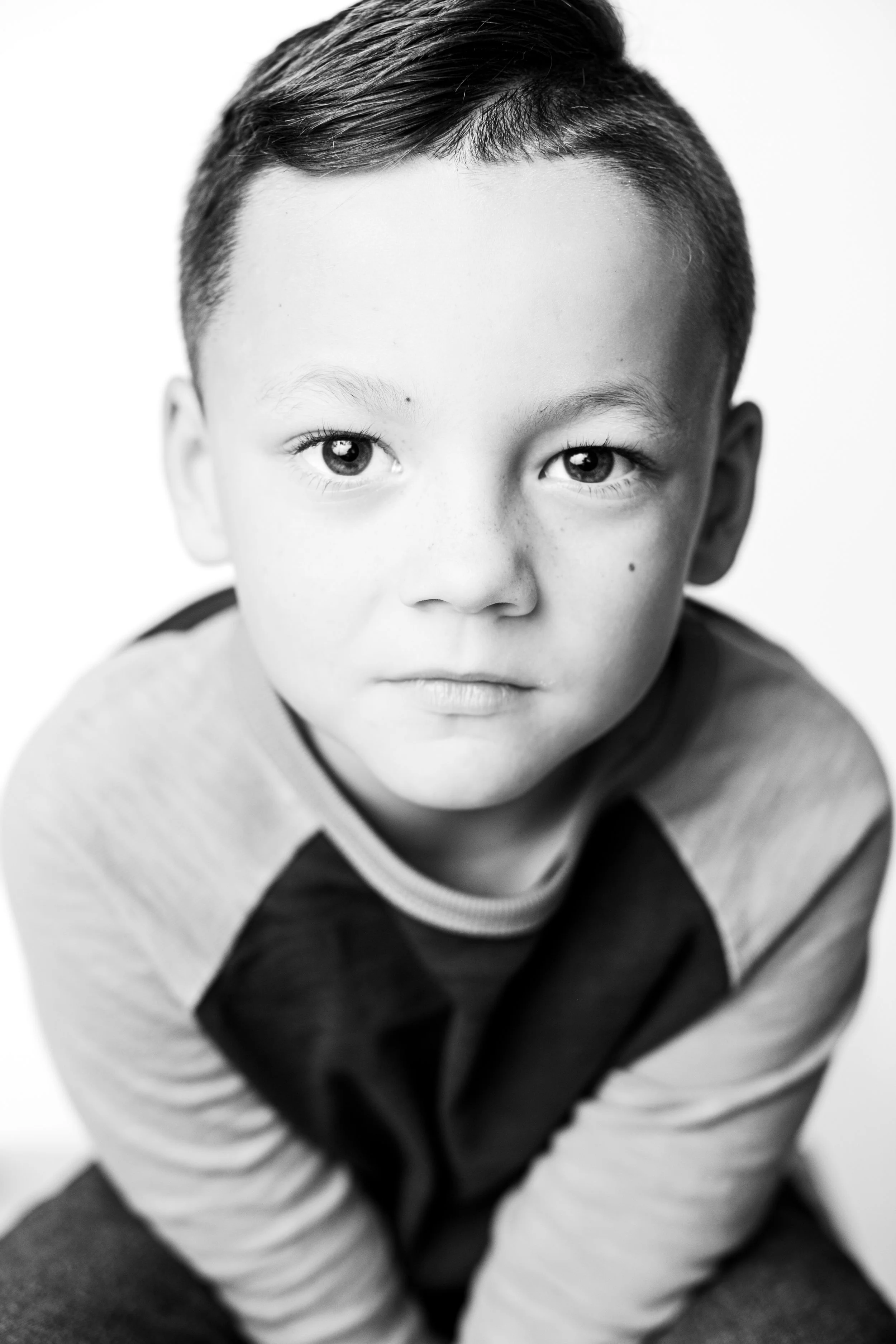 Black and white portrait of a young boy with short hair, looking directly at the camera with a serious expression, wearing a striped shirt.