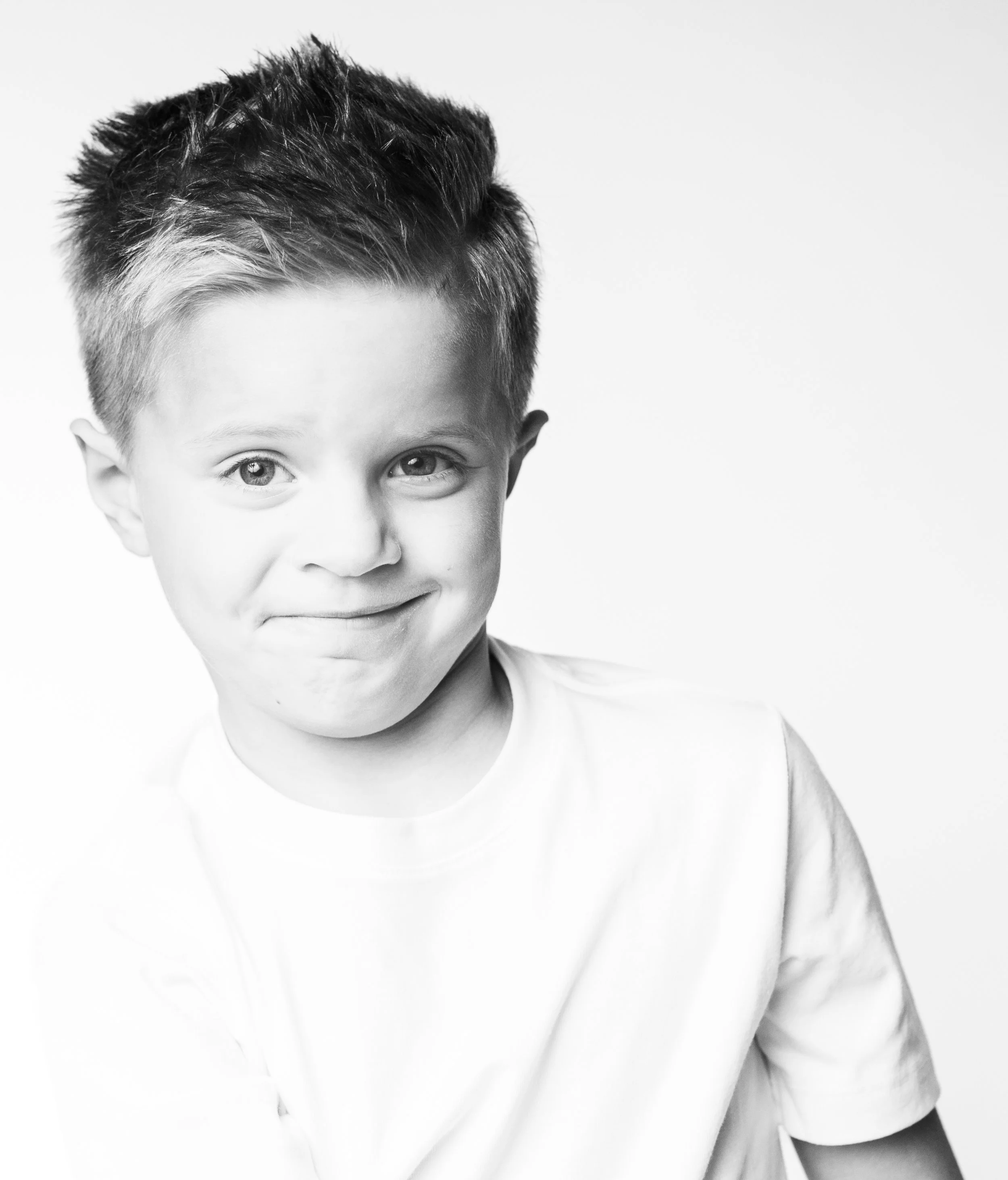 Black and white photo of a young boy with a slight smile, short spiked hair, wearing a plain t-shirt, looking directly at the camera.