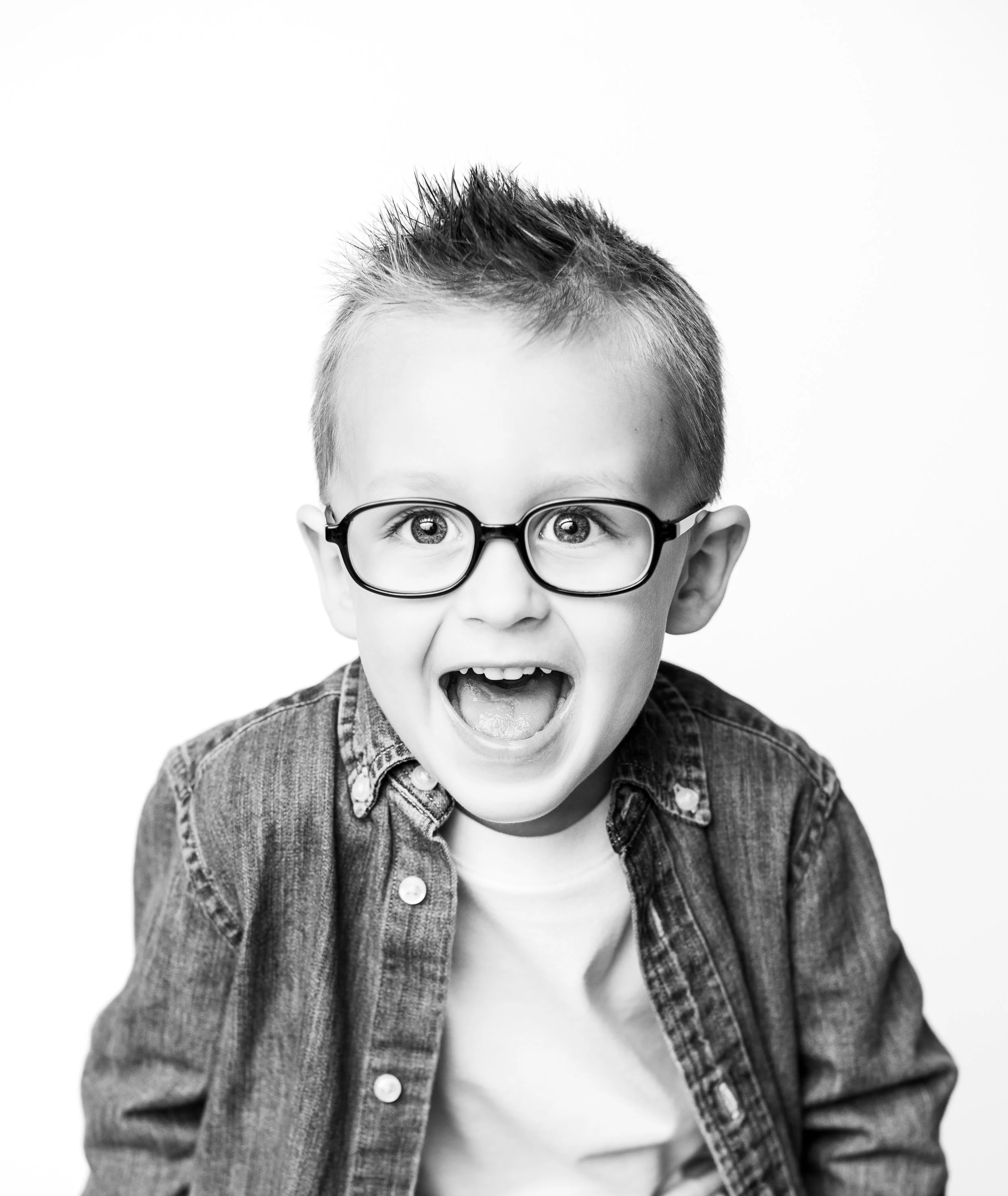 Black and white photo of a young boy with glasses, showing a surprised or excited expression.