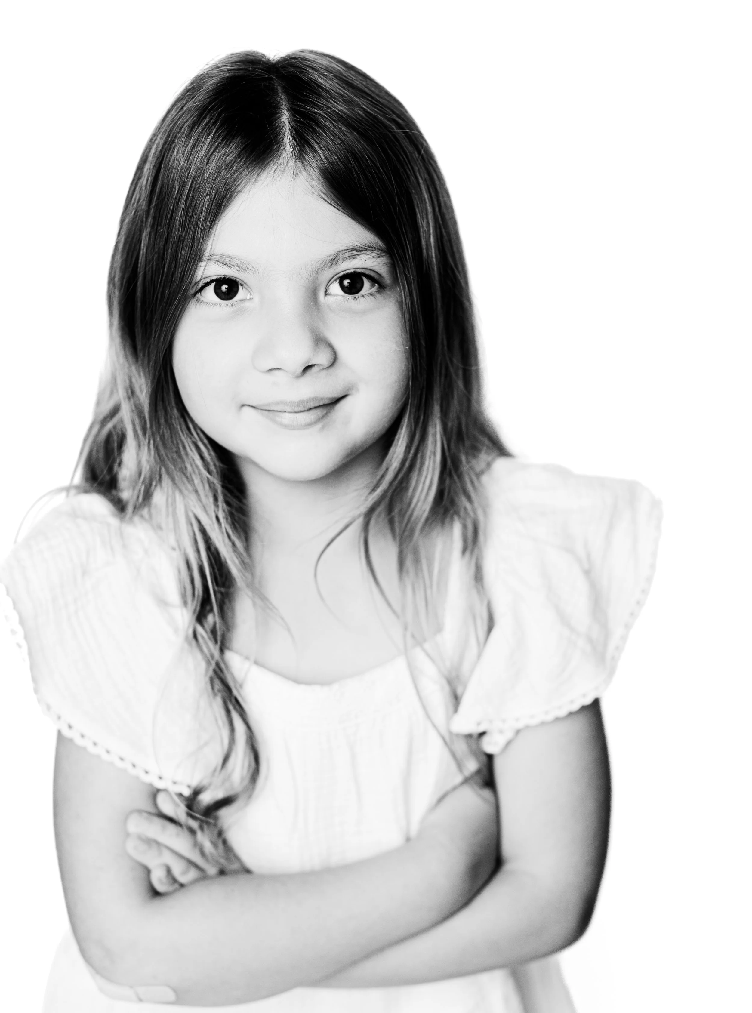 A young girl with long hair smiling, wearing a light-colored top with puffed sleeves, arms crossed, in black and white.